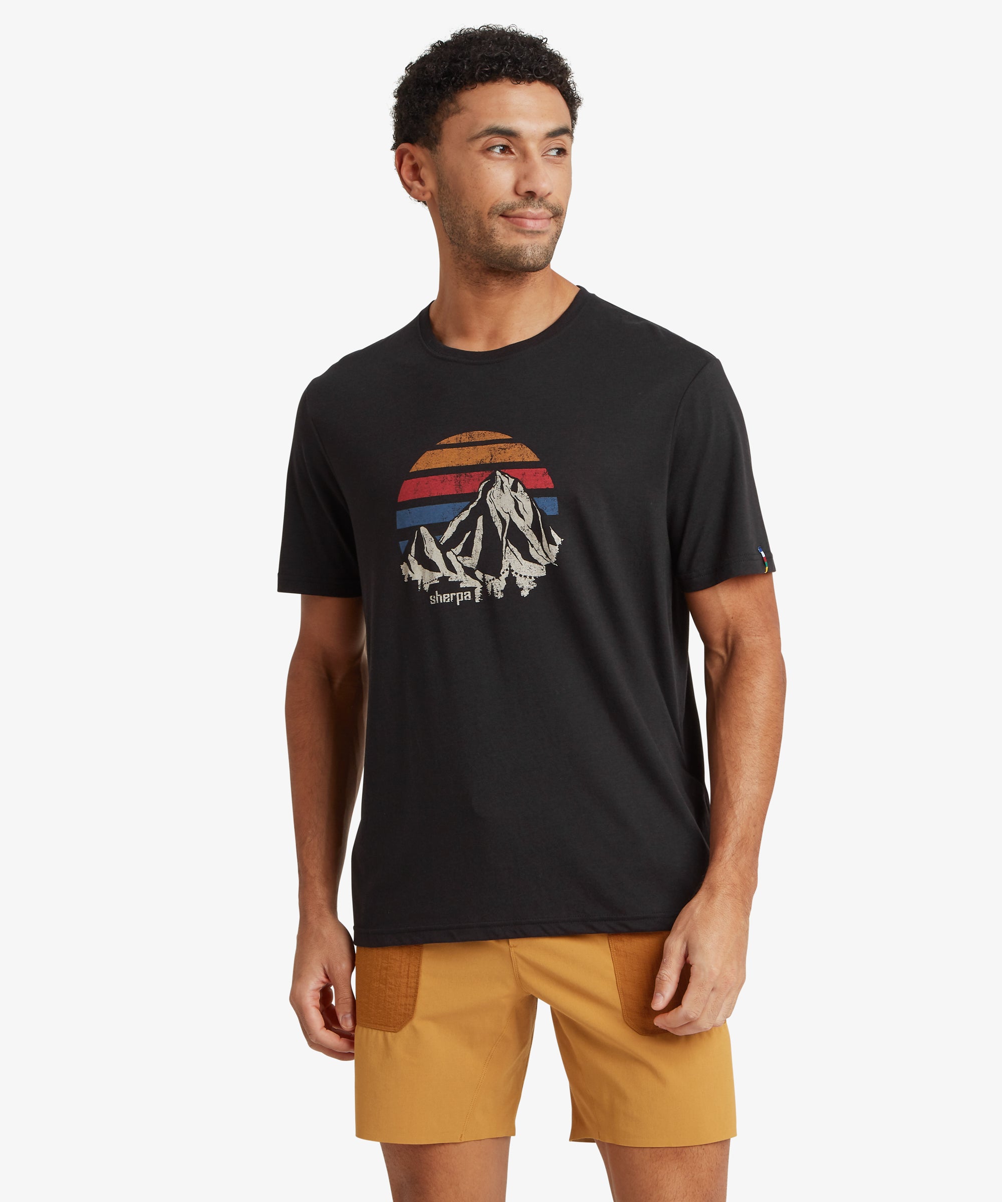 Front view of a person wearing a black graphic T‑shirt featuring a retro mountain and sunset print, paired with mustard shorts.