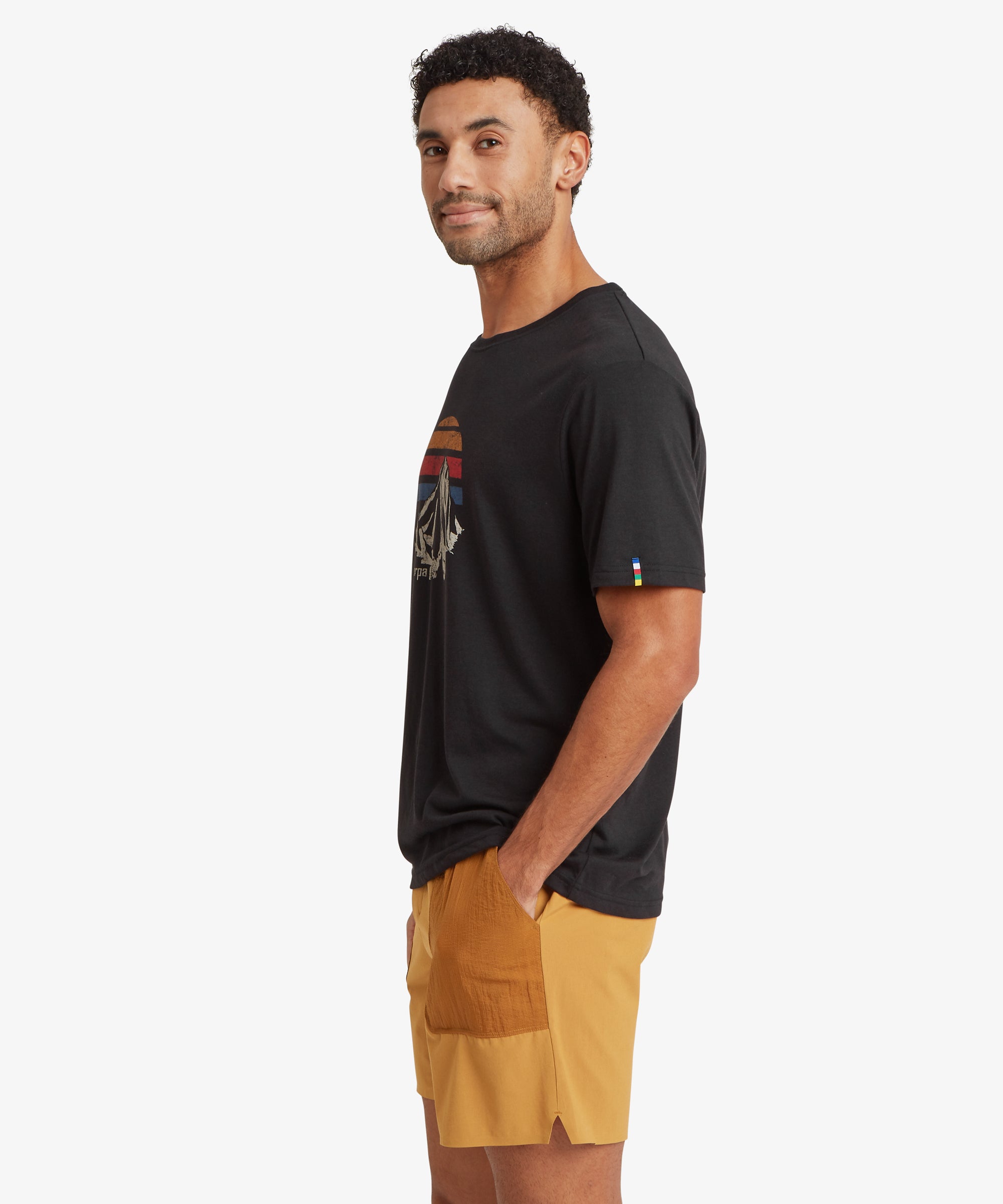 Side view of a person wearing a black T‑shirt with a retro mountain graphic and mustard shorts.