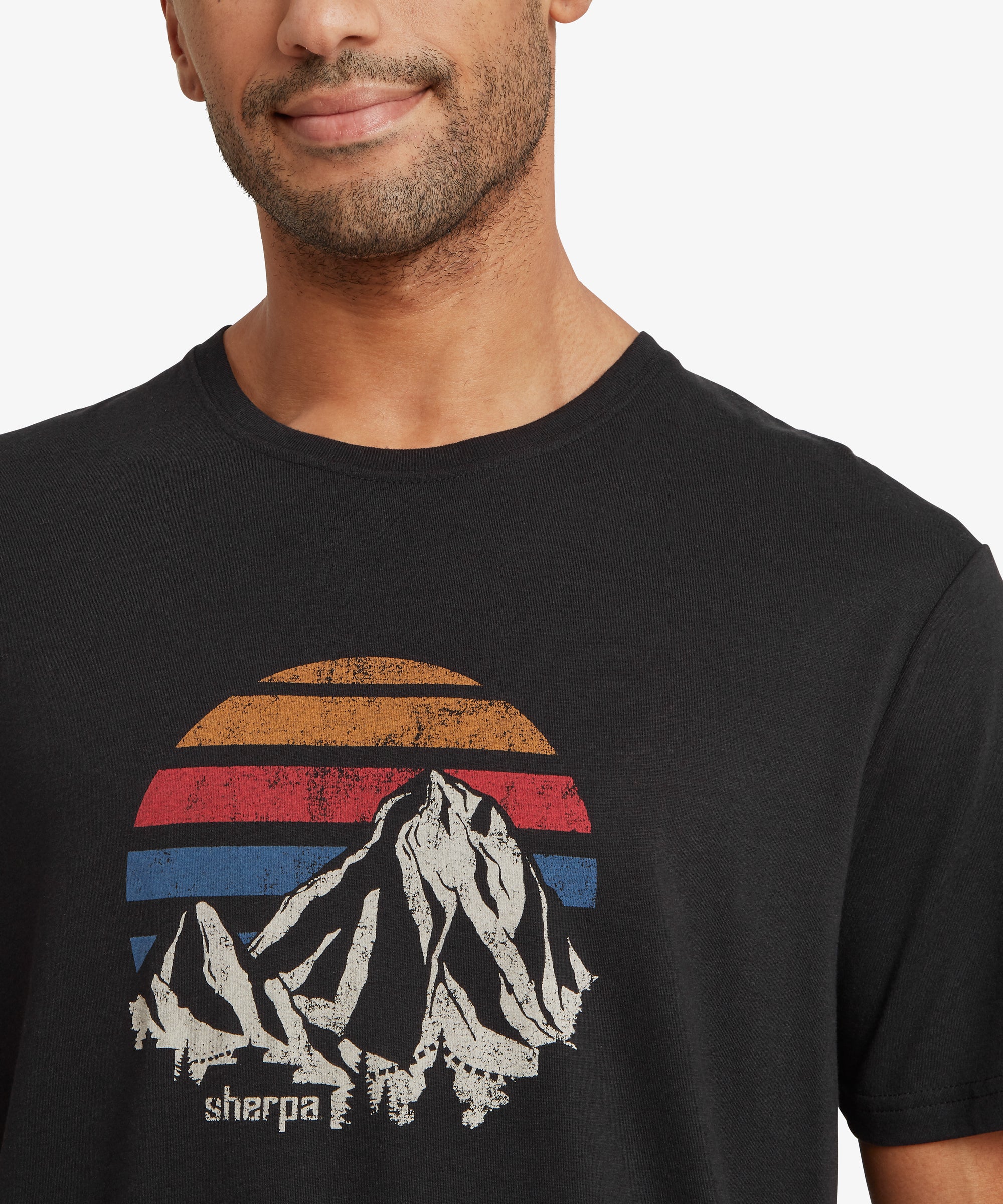 Close‑up of a black graphic T‑shirt with a retro mountain and sunset design and “sherpa” text.
