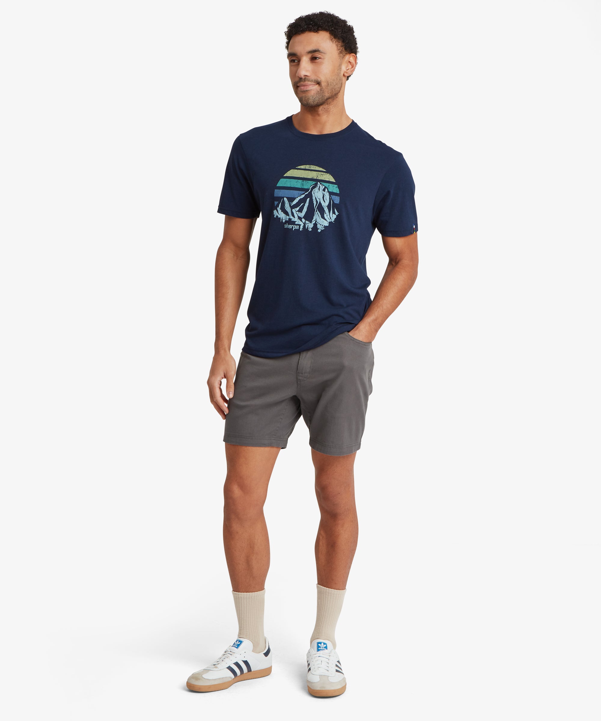 Full‑body front view of a person wearing a navy mountain‑graphic T‑shirt and grey shorts.