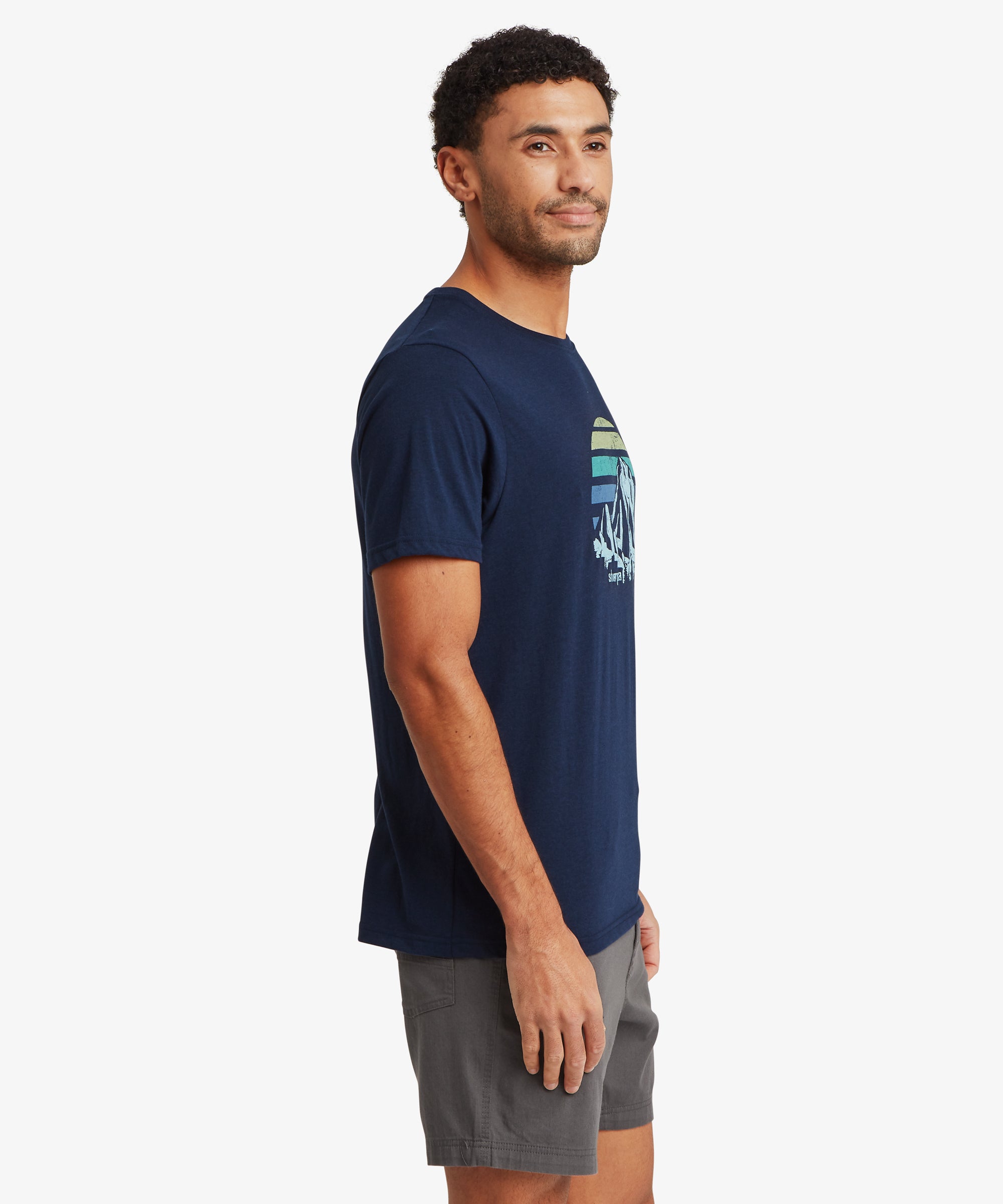 Side view of a person wearing a navy graphic T‑shirt with a retro mountain and striped horizon design, paired with grey shorts.