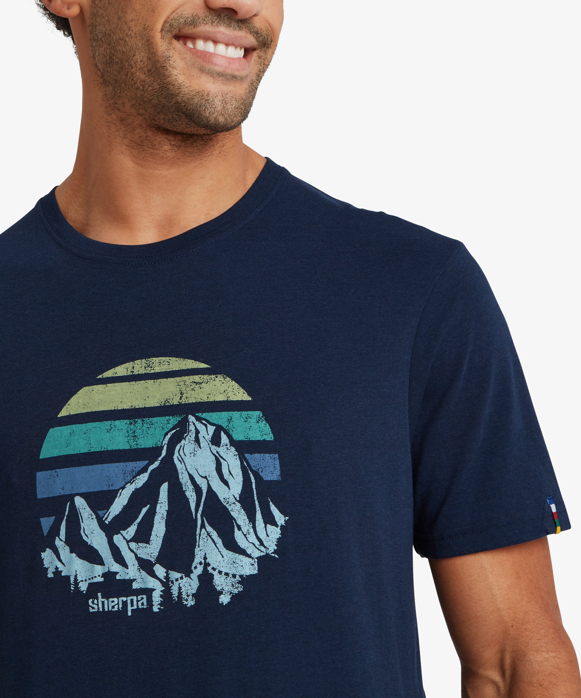 Close‑up of a navy graphic T‑shirt with a retro mountain and striped horizon print and “sherpa” text.