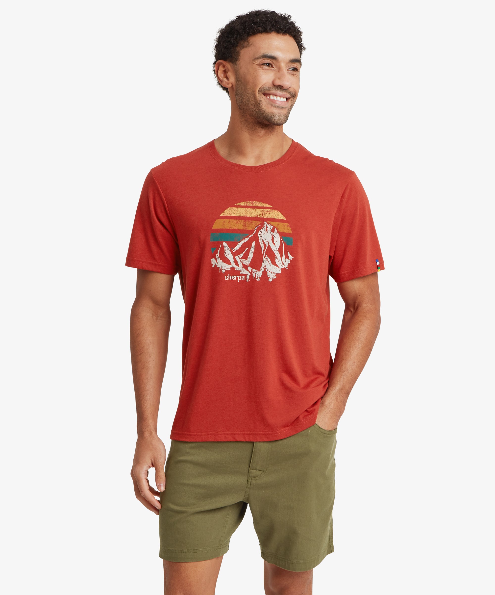 Front view of a person wearing a red graphic T‑shirt with a retro mountain and sunset print, paired with olive shorts.