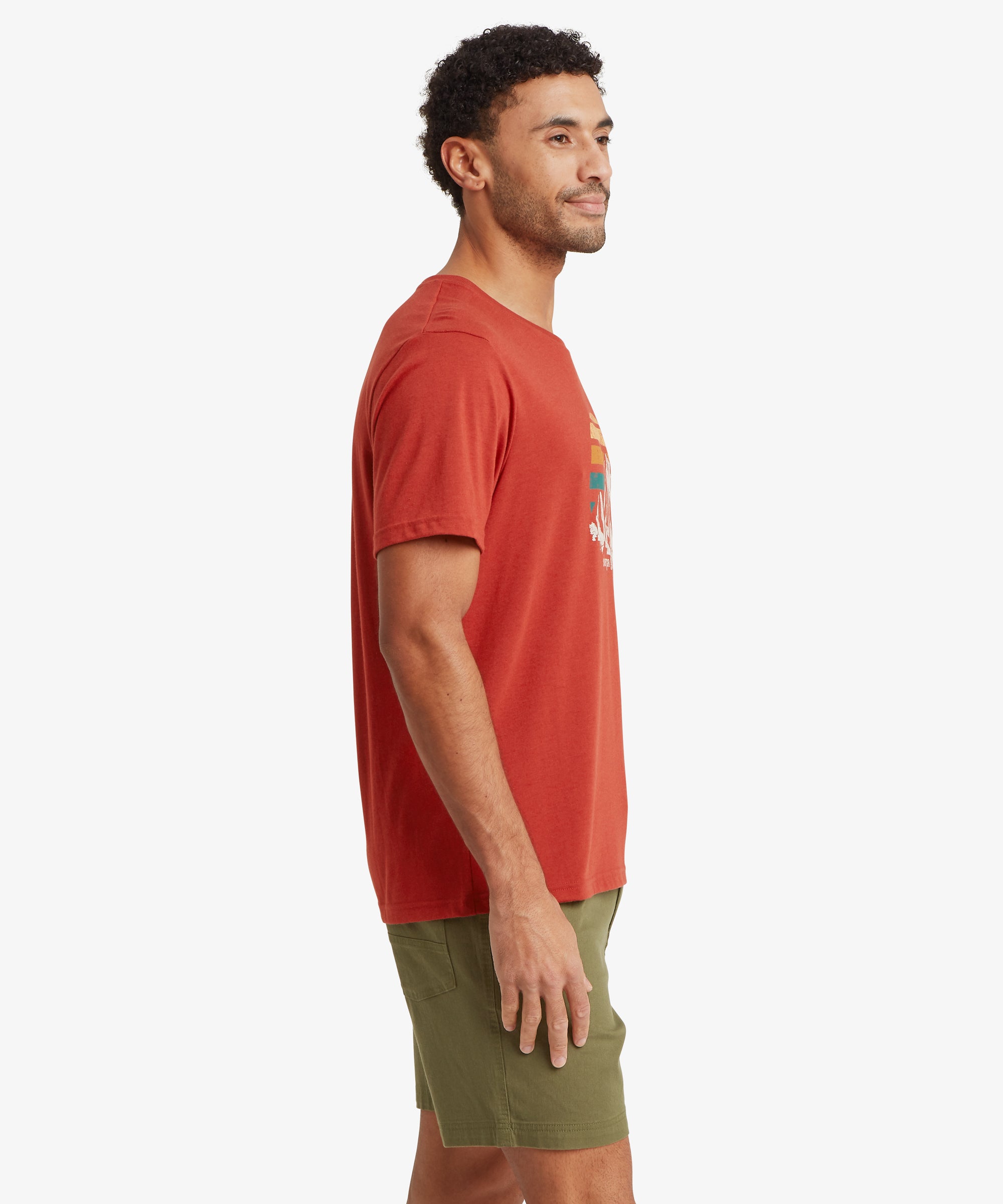Side view of a person wearing a red graphic T‑shirt with a retro mountain and sunset design, paired with olive shorts.