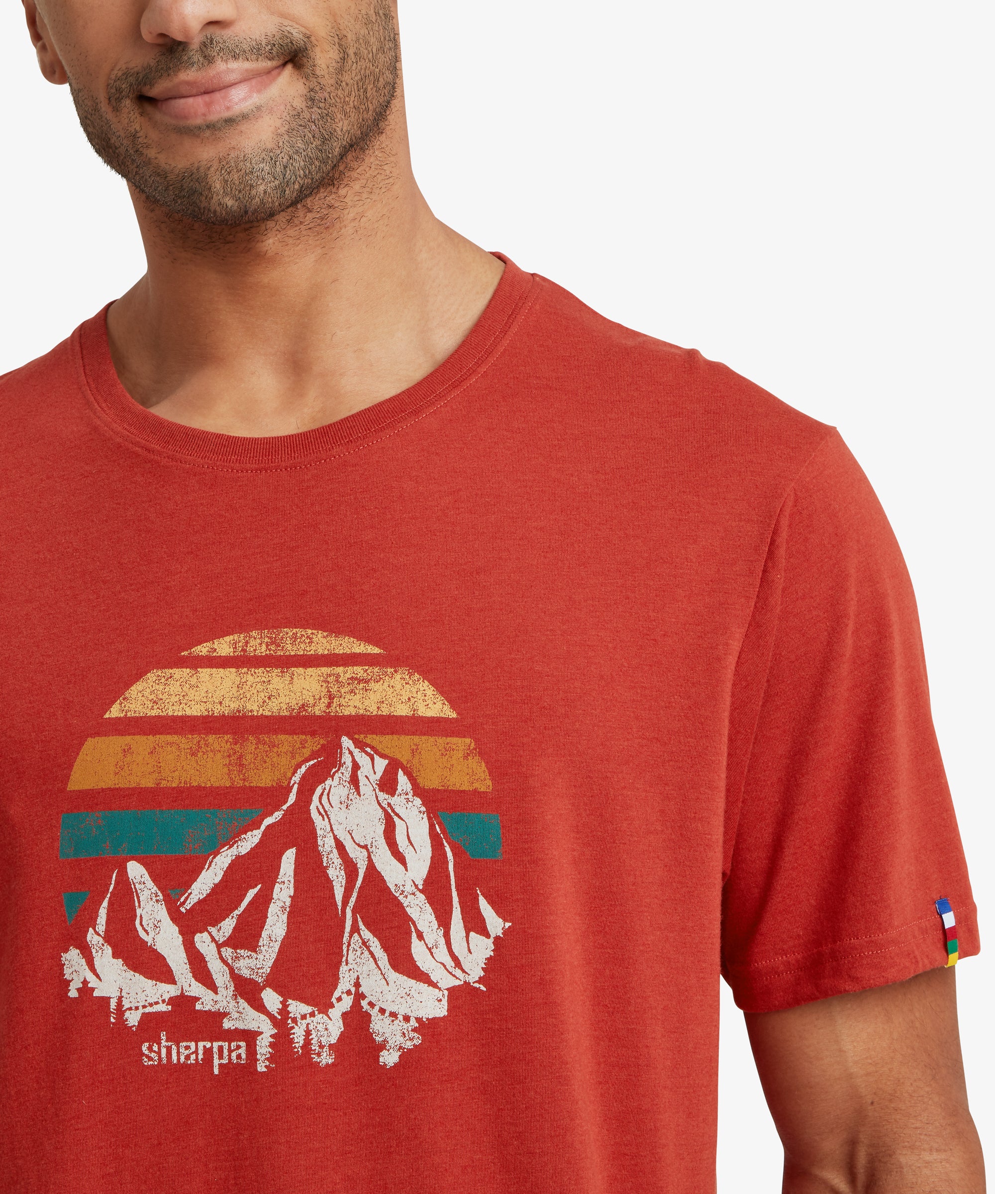 Close‑up of a red graphic T‑shirt featuring a retro mountain and sunset print with “sherpa” text.