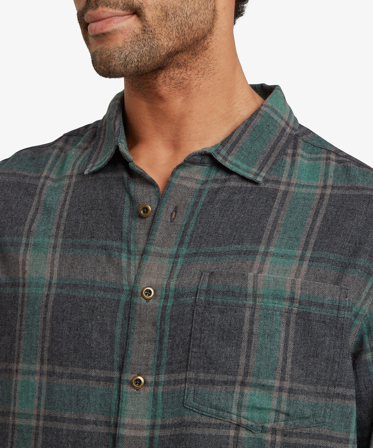 Close-up of a man wearing a long-sleeve button-up flannel shirt with a green.