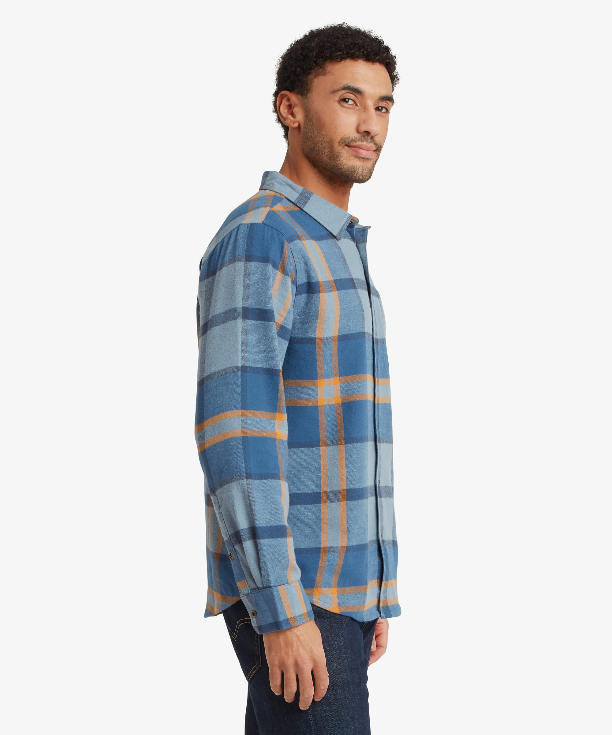 Side profile of a man wearing a blue plaid long-sleeve shirt showing the comfortable fit through the shoulders and torso, long sleeves and curved hem.