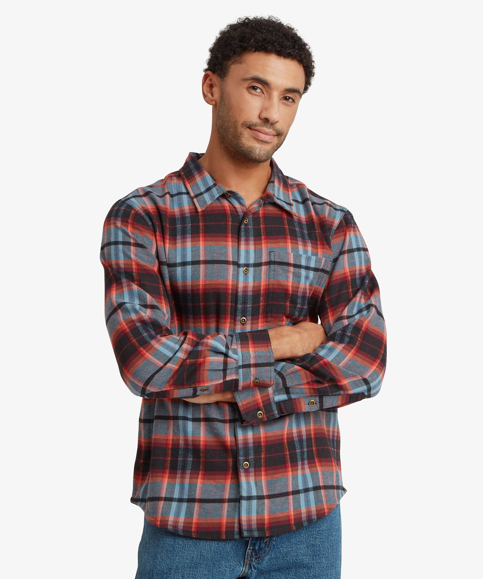Front view of a man wearing a red, navy and grey plaid long-sleeve shirt featuring a classic collar, button-front closure and chest pocket. He stands with his arms folded, highlighting the relaxed fit.