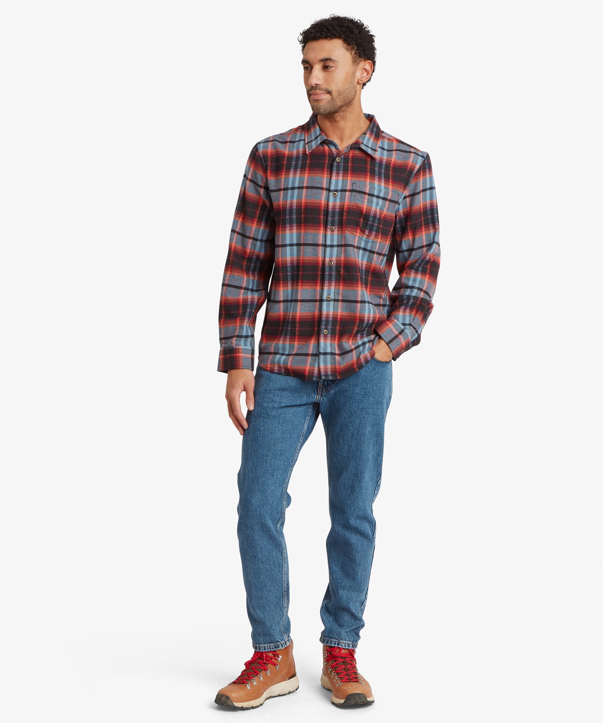 Full-body view of a man wearing a red plaid long-sleeve shirt with a relaxed fit through the body and sleeves. The shirt is paired with blue jeans and casual shoes.