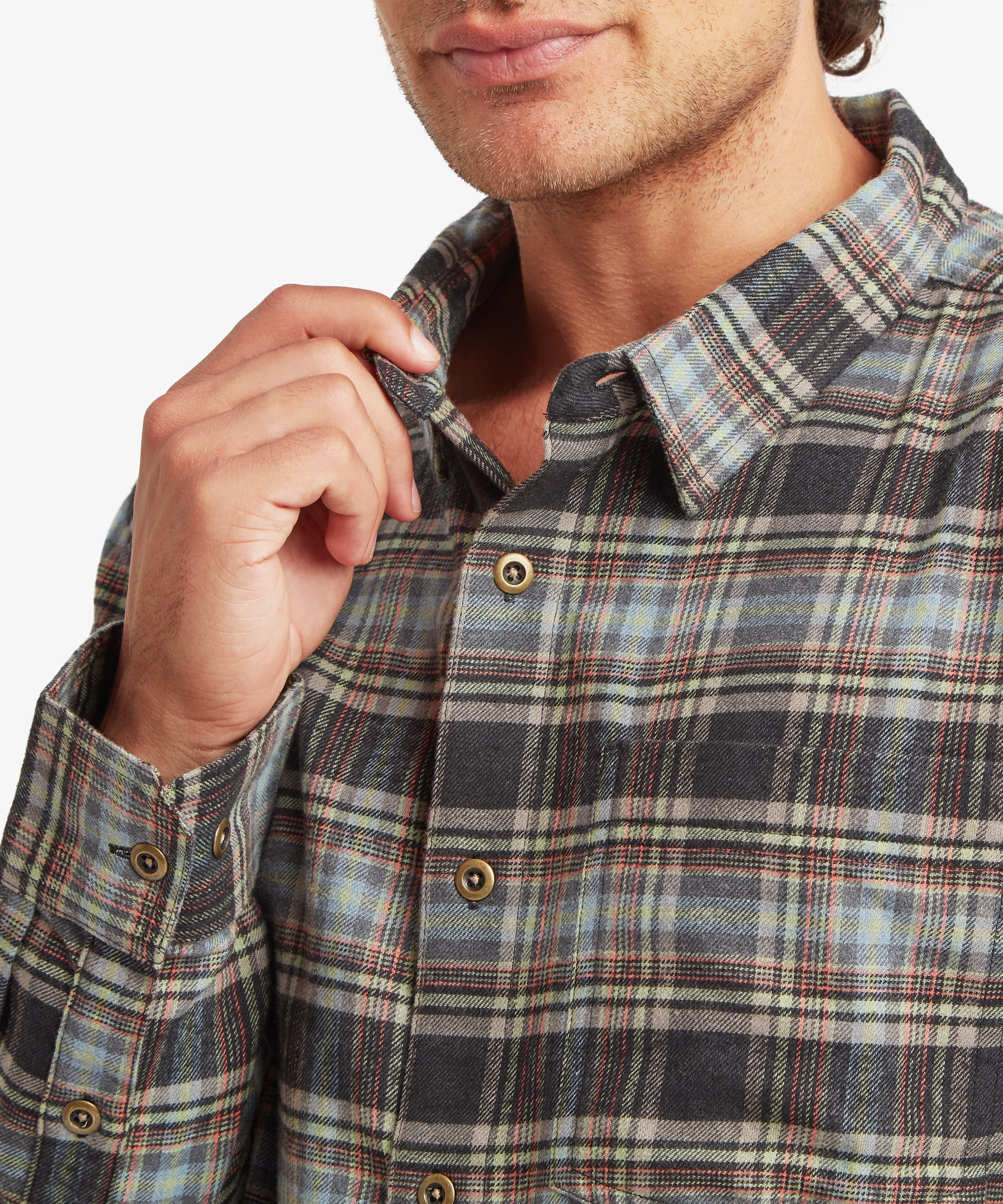 Close-up of the collar and upper chest of an olive and brown plaid shirt. Details include natural-look buttons, a spread collar, soft brushed fabric texture and a plaid pattern combining olive green, cream, brown and charcoal stripes. The man lightly holds the collar with one hand.