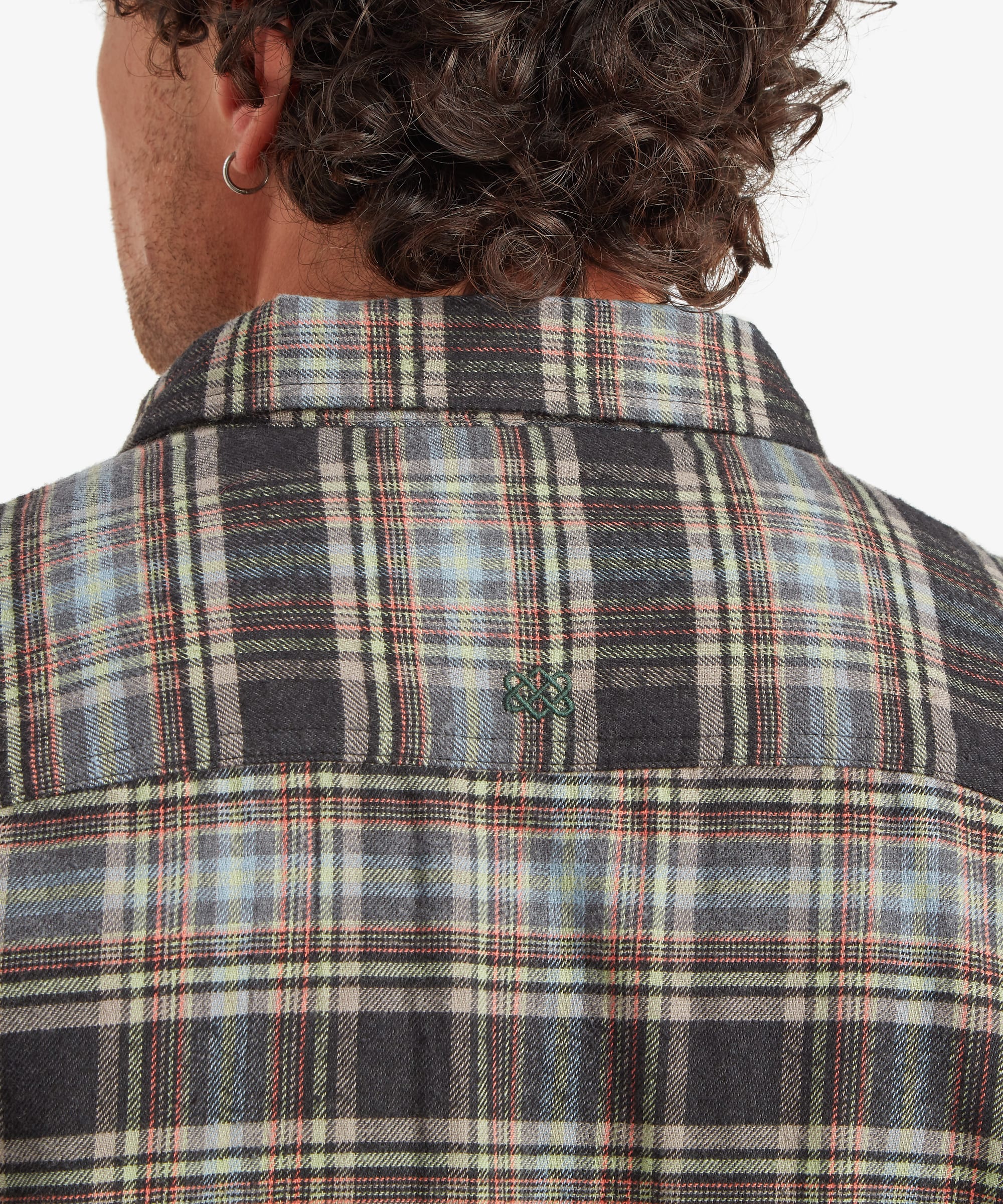 Close-up back view of the plaid shirt showing the back yoke construction, centred locker loop detail and the intersecting olive, cream, brown and charcoal plaid pattern across the shoulders.