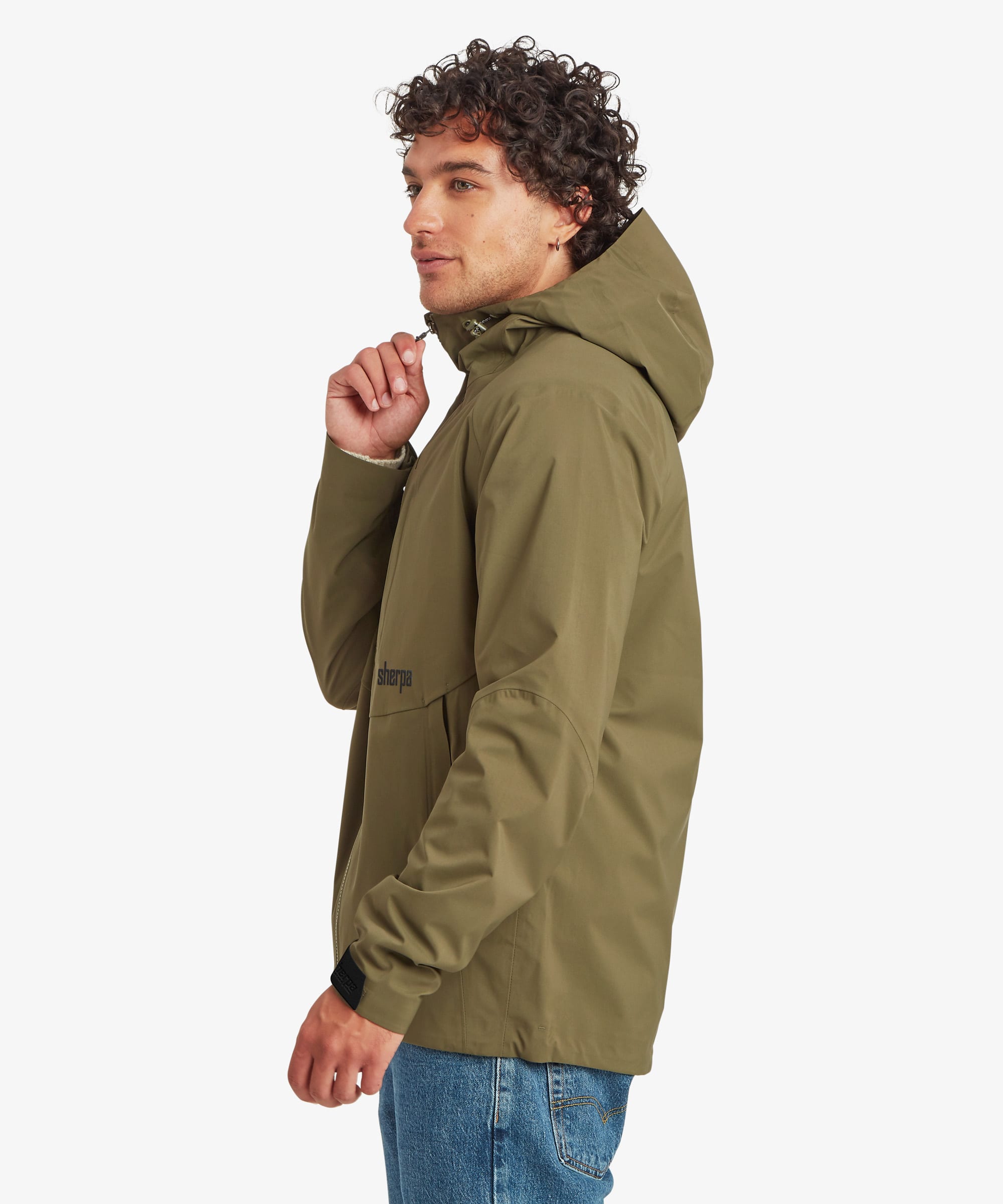 A half length portrait of a man wearing an olive green waterproof hooded jacket, shown in profile against a light gray background. The man is adjusting the zip of the jacket.