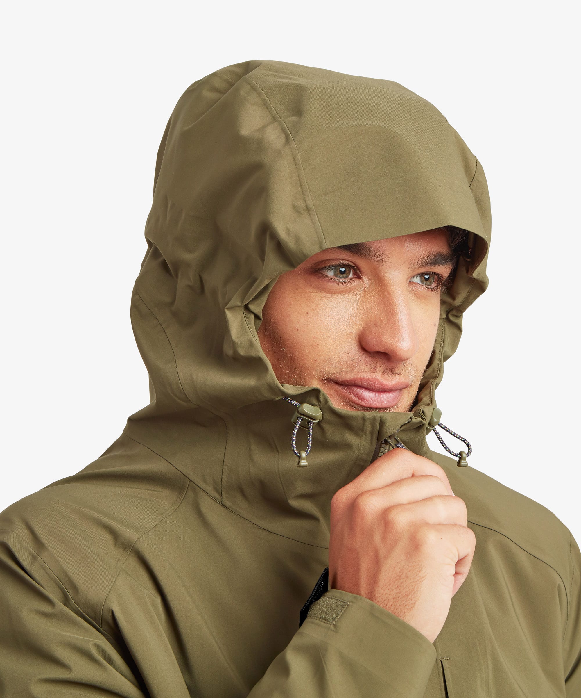 A close up of a man wearing a green Sherpa Adventure Gear waterproof jacket. The man has the hood of the jacket over his head and is adjusting the zip with his right hand.