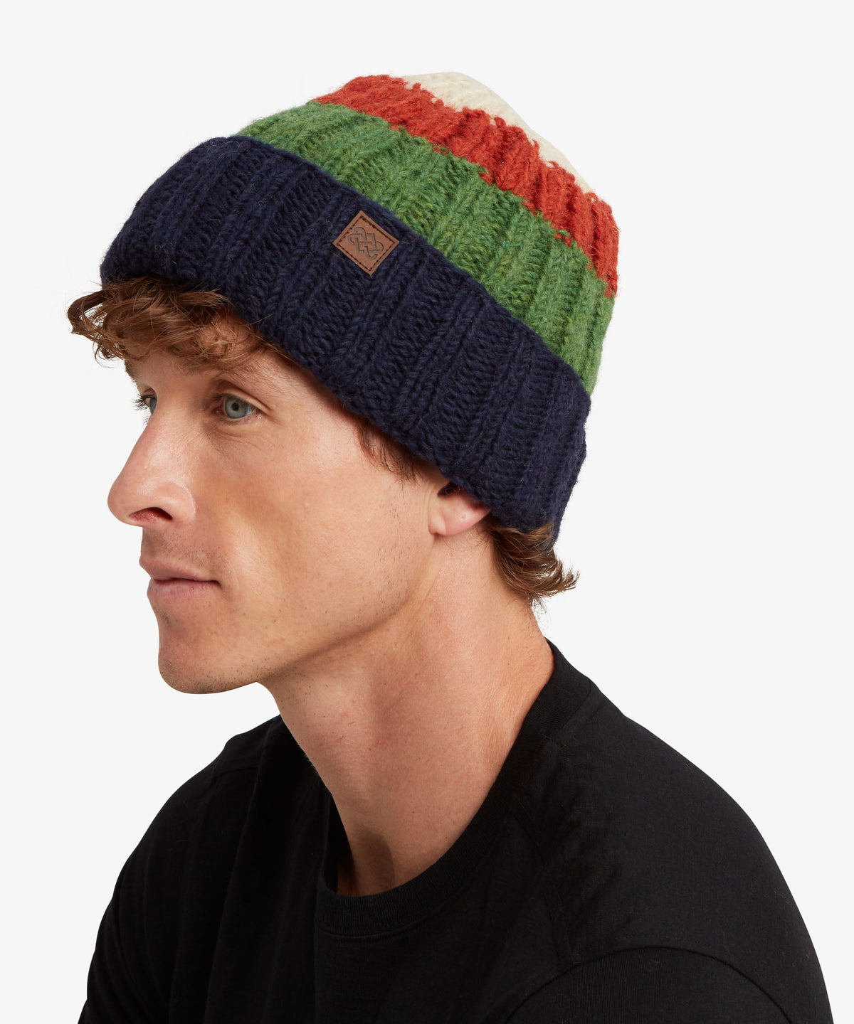 A man in a black t-shirt wearing a multi-colored knit beanie with navy blue, green, rust red.
