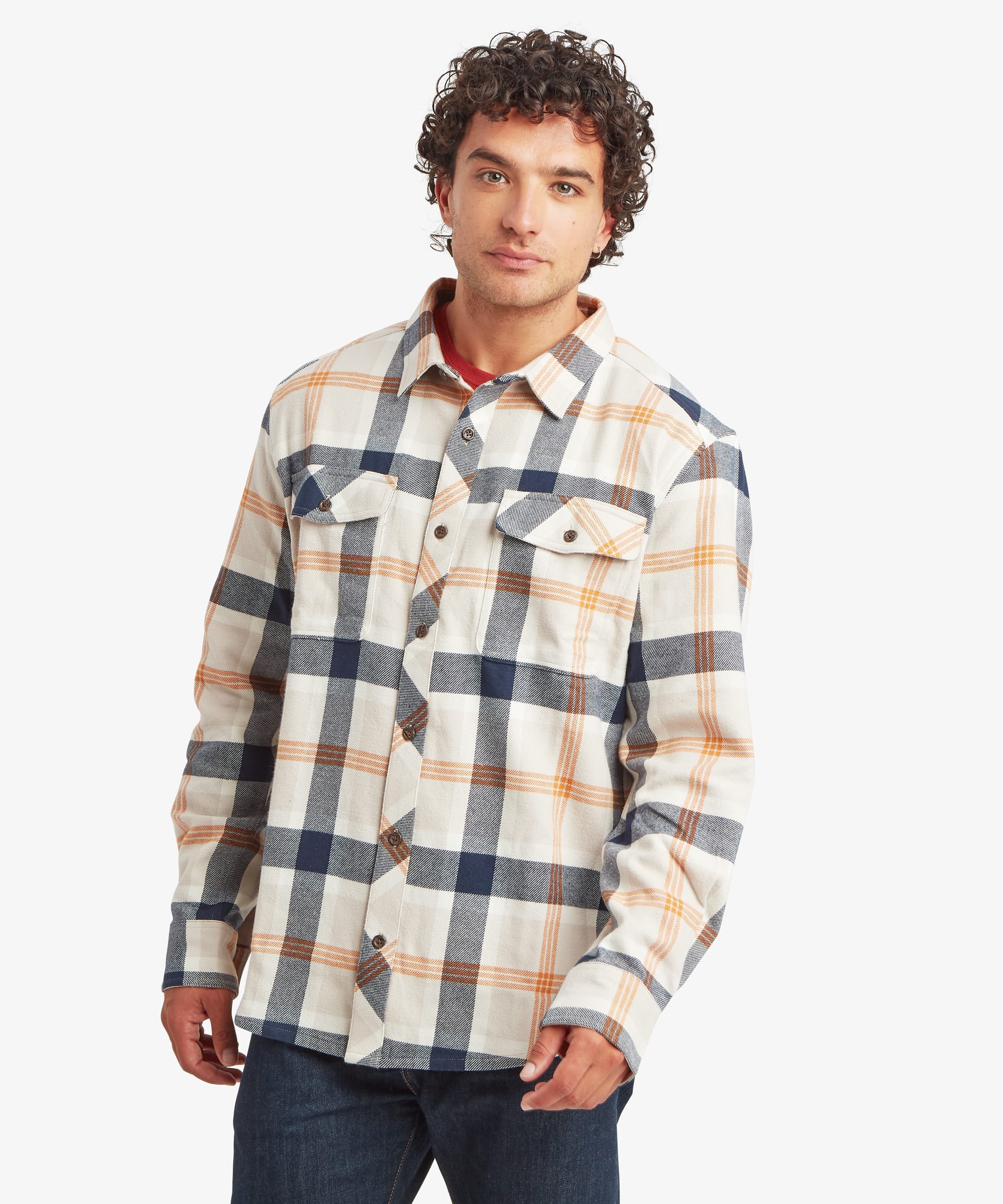 Front view of a man wearing a long-sleeve plaid overshirt in cream, navy and warm tan tones. The shirt features a relaxed fit, button-front closure, spread collar and two button-flap chest pockets. The man stands casually with a neutral expression.