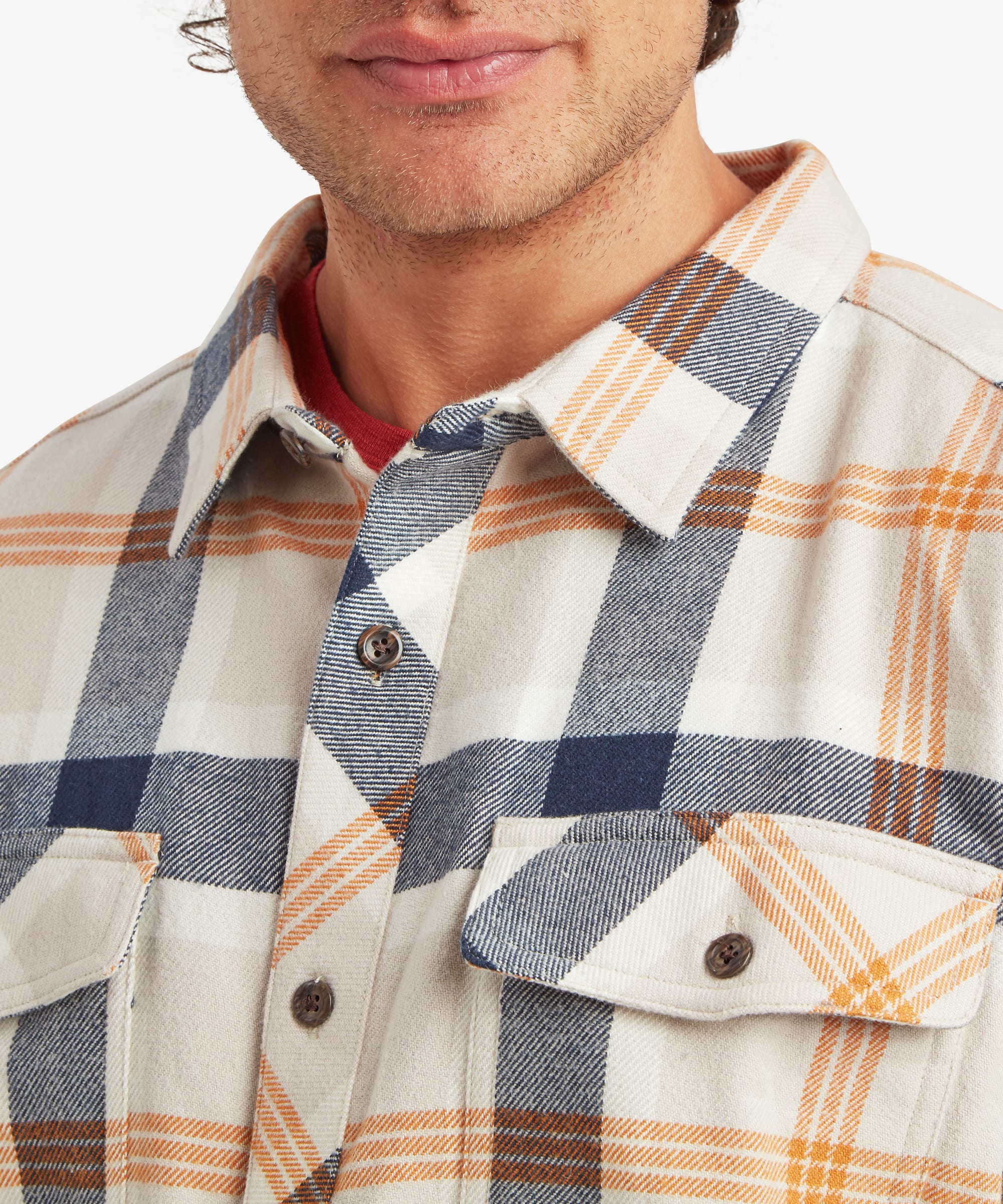 Close-up of the chest area of a cream plaid overshirt showing two button-flap chest pockets, natural-look buttons, a spread collar and large-scale navy and tan check pattern.