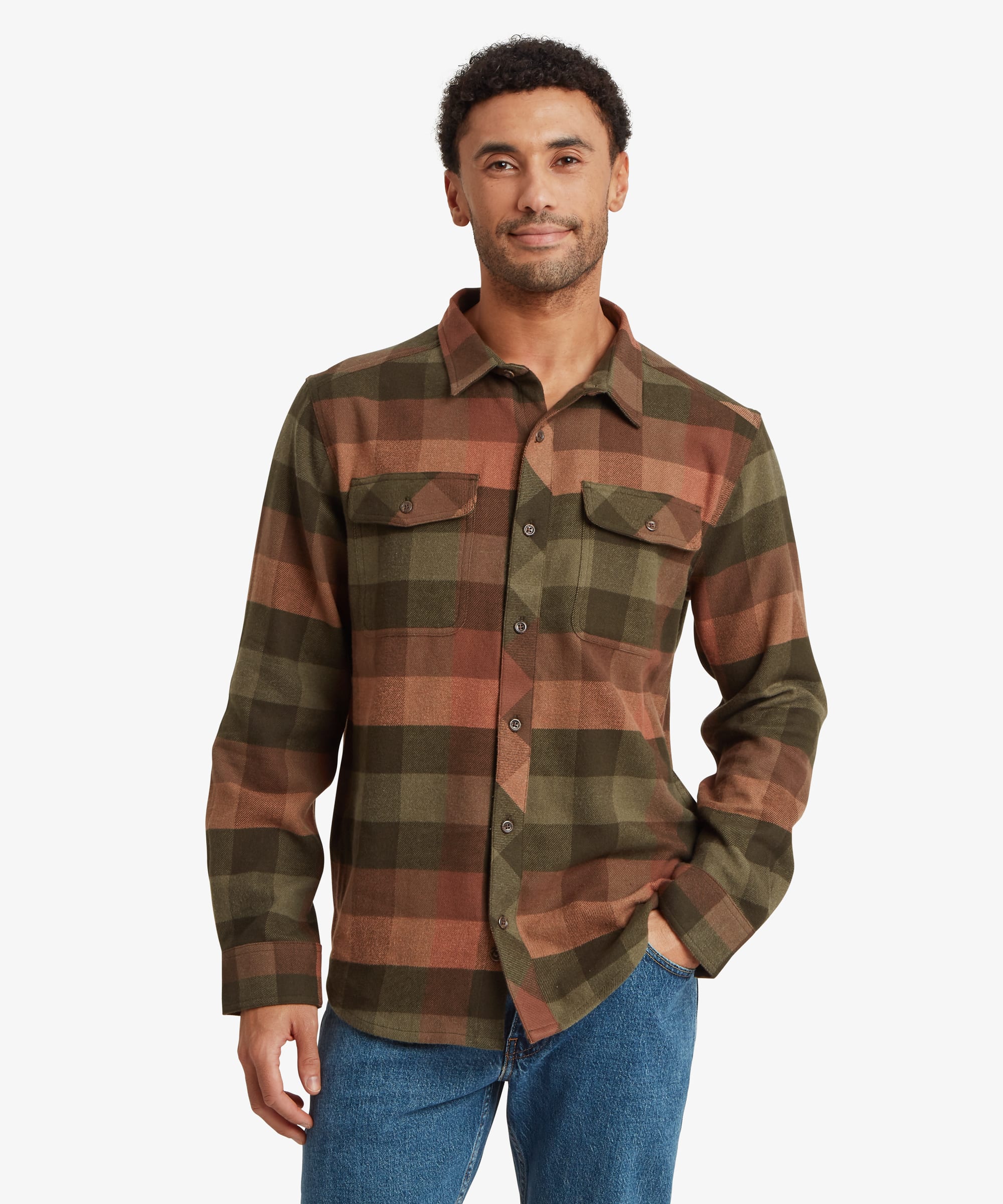 Front view of a man wearing a long-sleeve plaid overshirt in olive green, rust brown and dark charcoal tones. The relaxed-fit shirt features a button-front closure, spread collar and two button-flap chest pockets. One hand rests casually in a pocket.