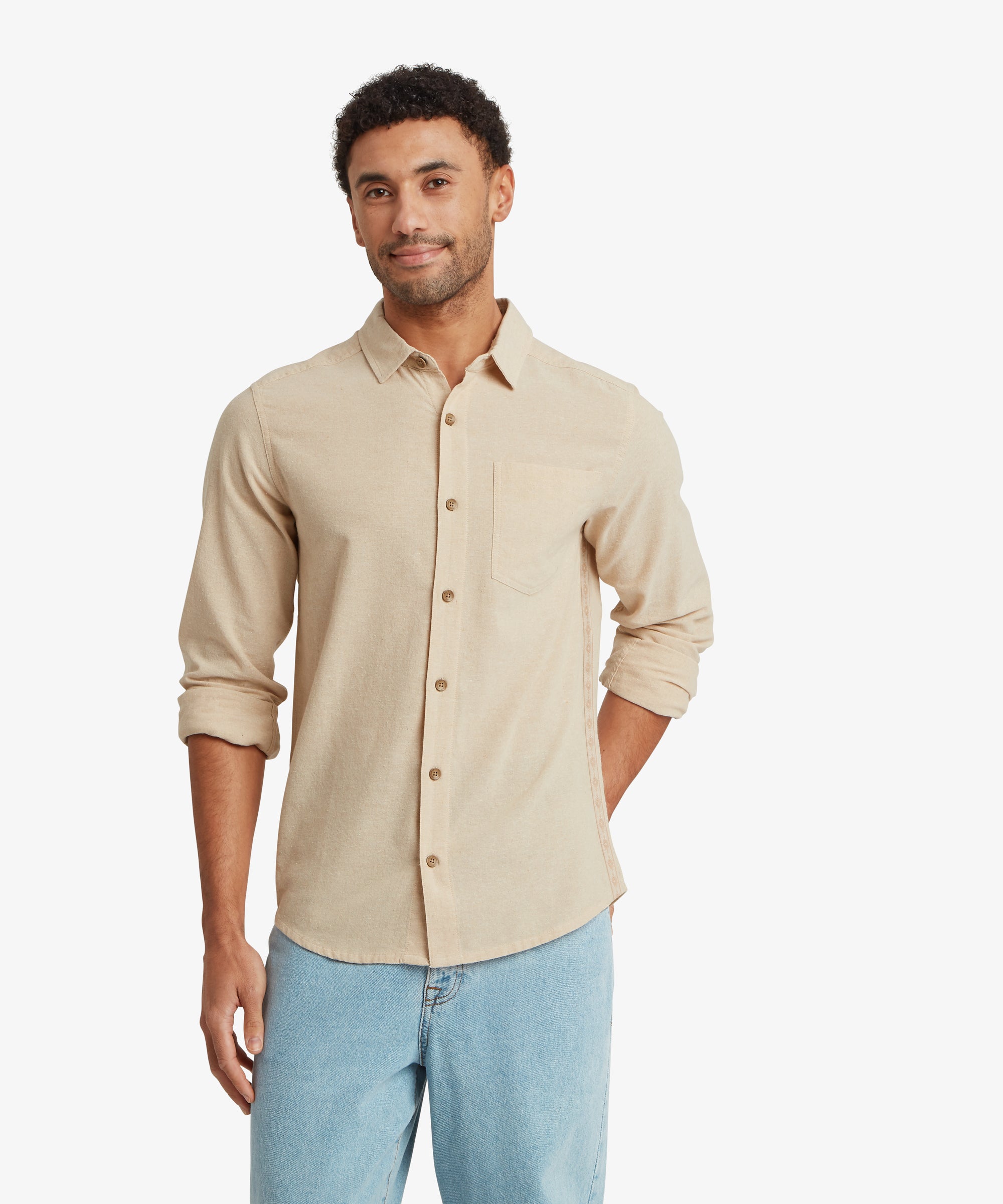 A front view of the beige long‑sleeve button‑up shirt with a chest pocket and tonal buttons. The shirt is worn untucked with light blue jeans, and one sleeve is slightly rolled.