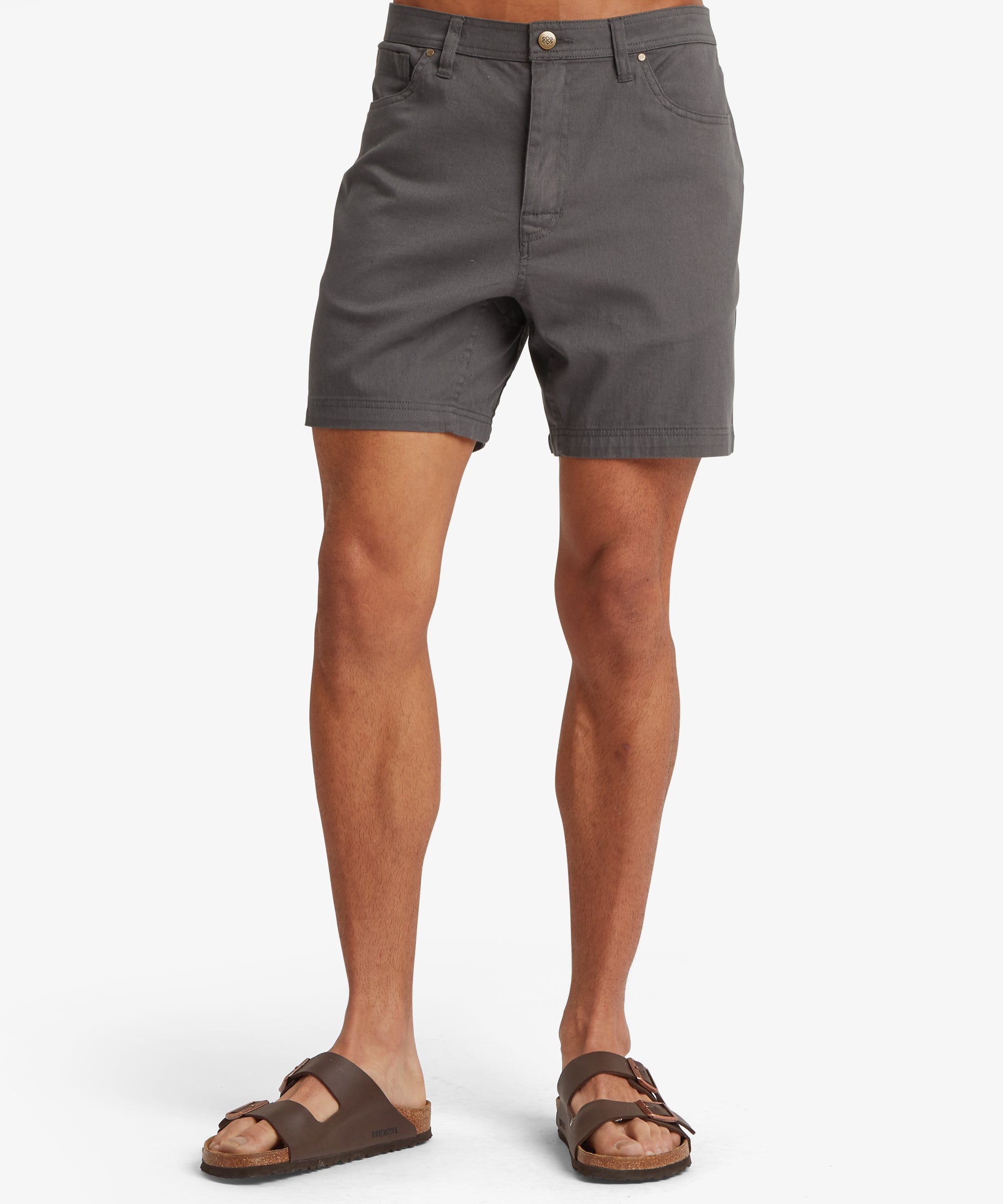 A front view of charcoal-grey 5‑pocket shorts featuring a structured waistband, button-and-zip closure, belt loops, and a straight hem, worn with brown double‑strap sandals.