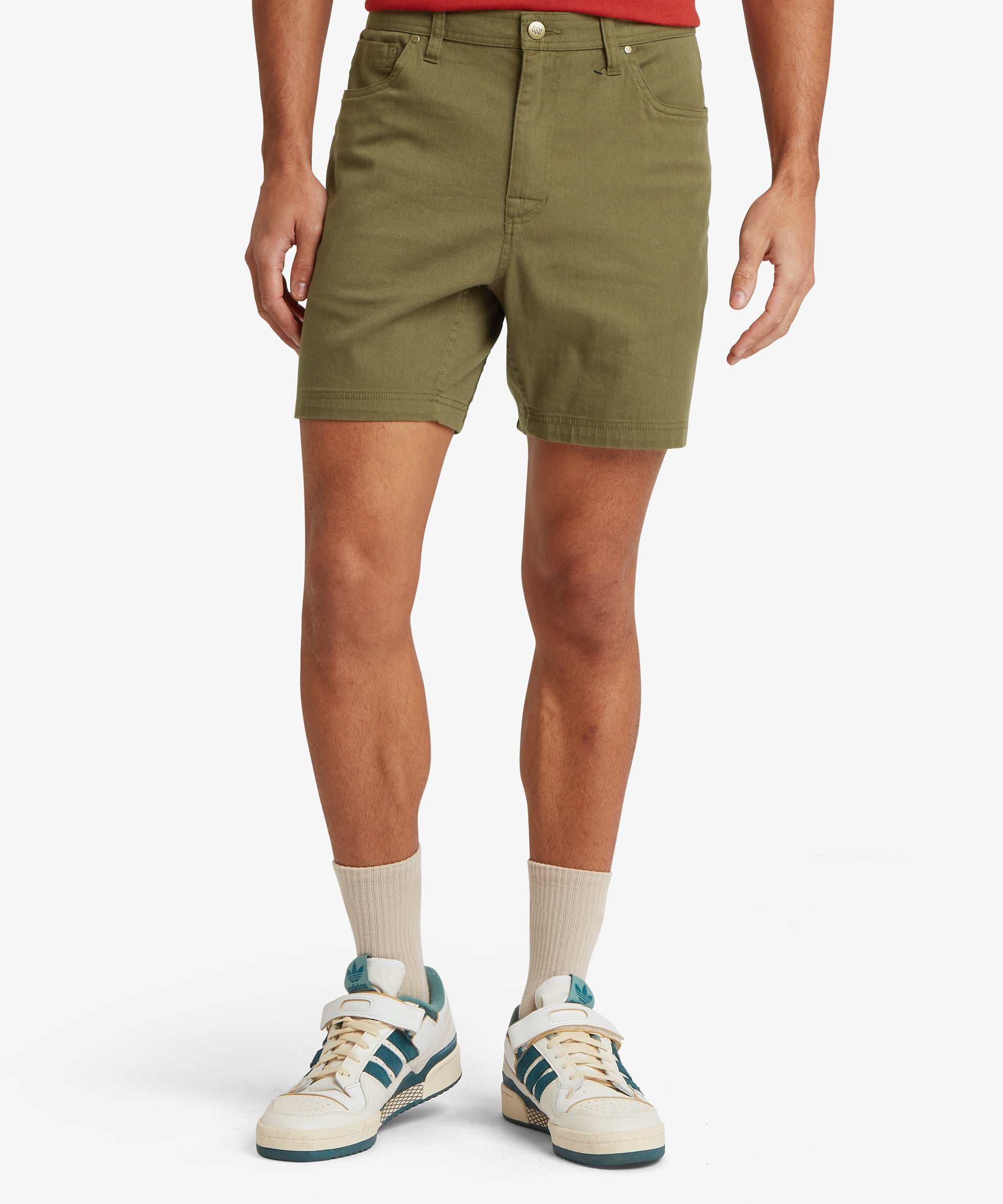 A front view of olive-green shorts featuring a classic 5‑pocket layout, structured waistband, and mid-thigh hem, styled with off‑white trainers and socks.
