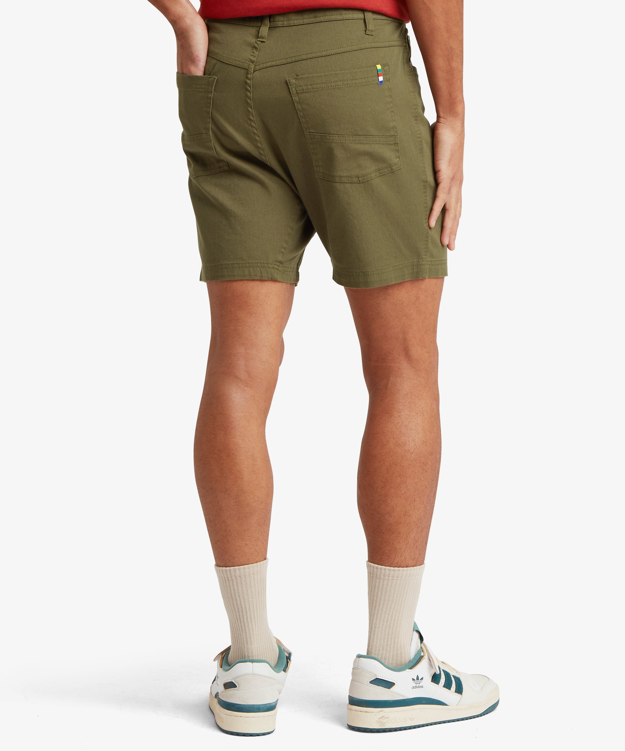 A back view of olive-green shorts showing two patch pockets with reinforced seam detailing and a multicolour woven tab.