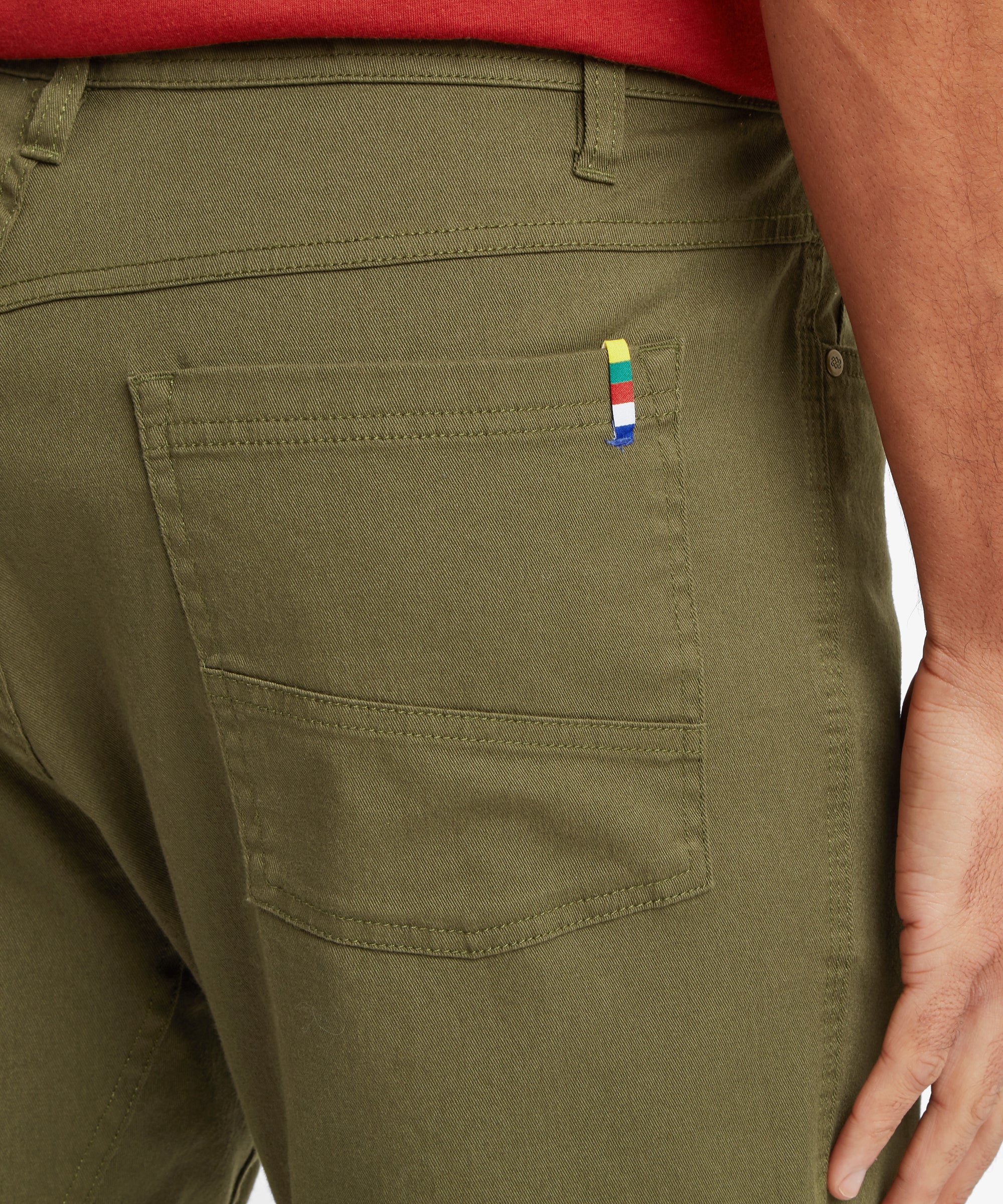 A close-up of the back pocket on olive shorts showing reinforced stitching and a multicolour woven tab for detail.
