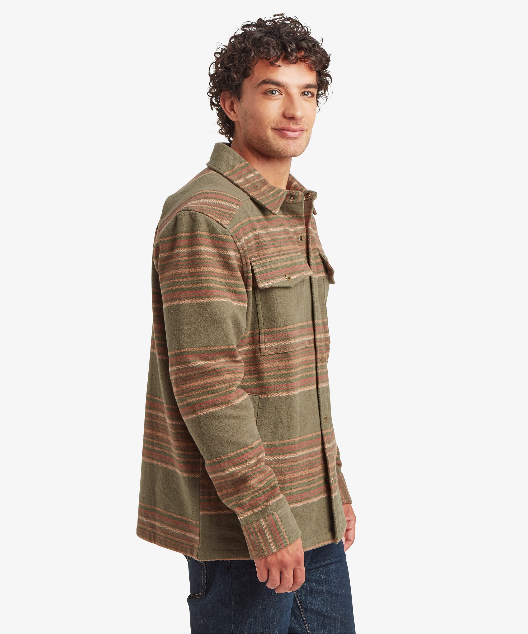 Side profile of a man wearing a relaxed-fit shirt jacket in olive green with rust, tan and charcoal stripe detailing across the chest and sleeves. The shirt jacket features long sleeves, button cuffs and a straight hem.