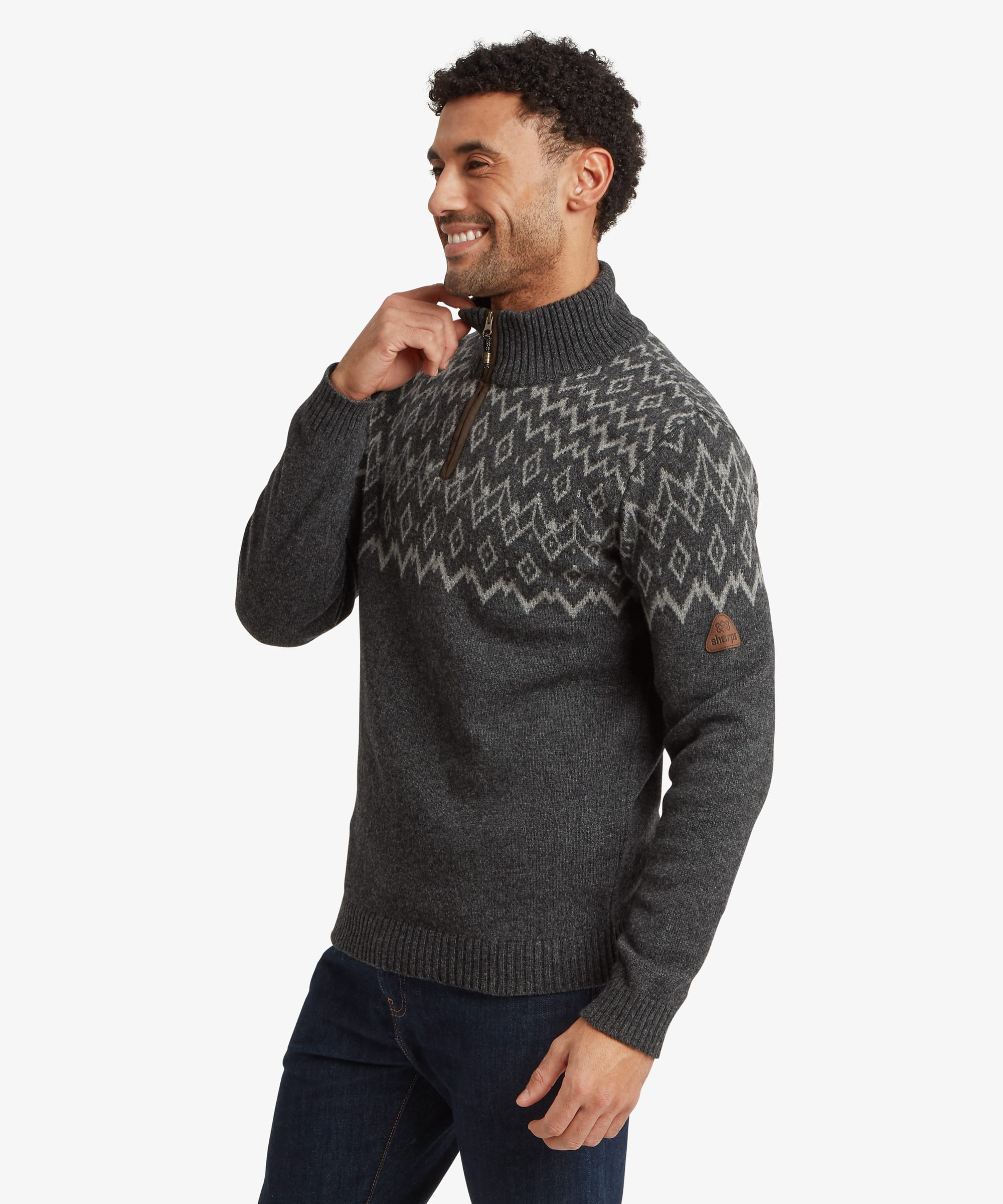 Side profile of a man wearing a charcoal grey quarter-zip sweater. The high collar, ribbed knit construction and patterned yoke design wrapping around the shoulders are visible. The man smiles while lightly touching the collar.