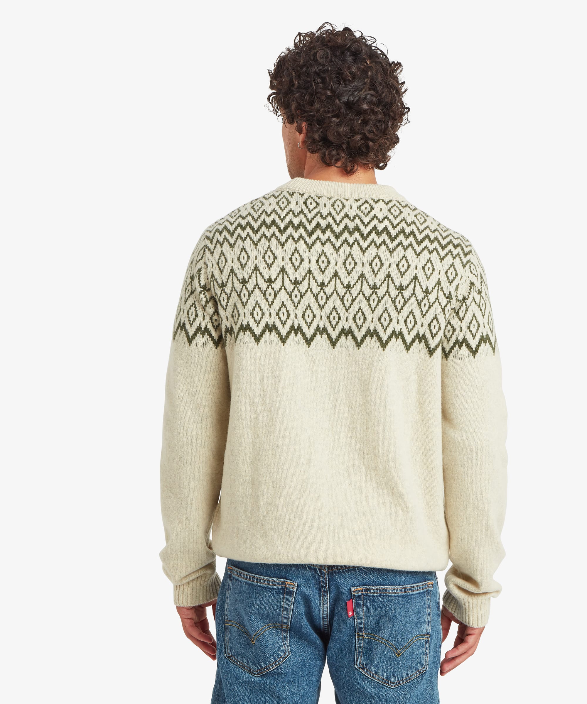 Rear view of a man wearing a cream crew neck sweater with an olive and charcoal geometric knit pattern extending across the shoulders and upper back. The regular-fit silhouette falls comfortably through the body and is paired with blue jeans. Ribbed trims finish the hem, cuffs and neckline.