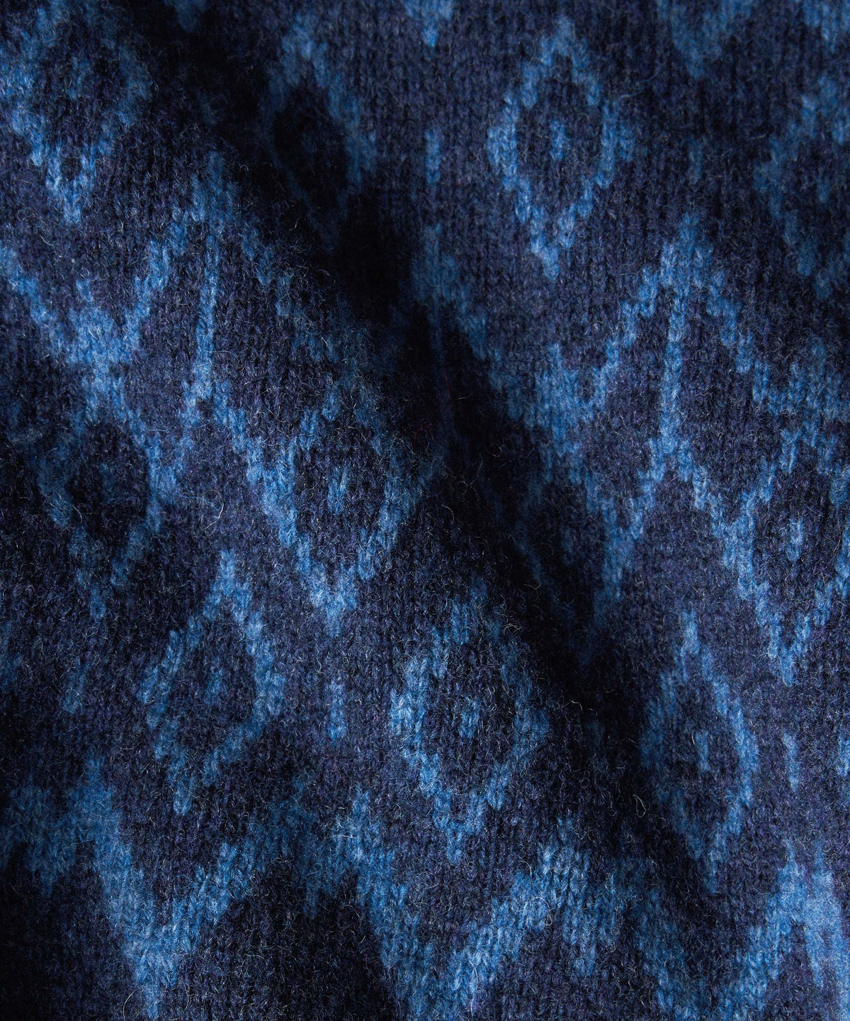 Close-up of a knitted fabric with a repeating diamond pattern in shades of navy and medium blue.