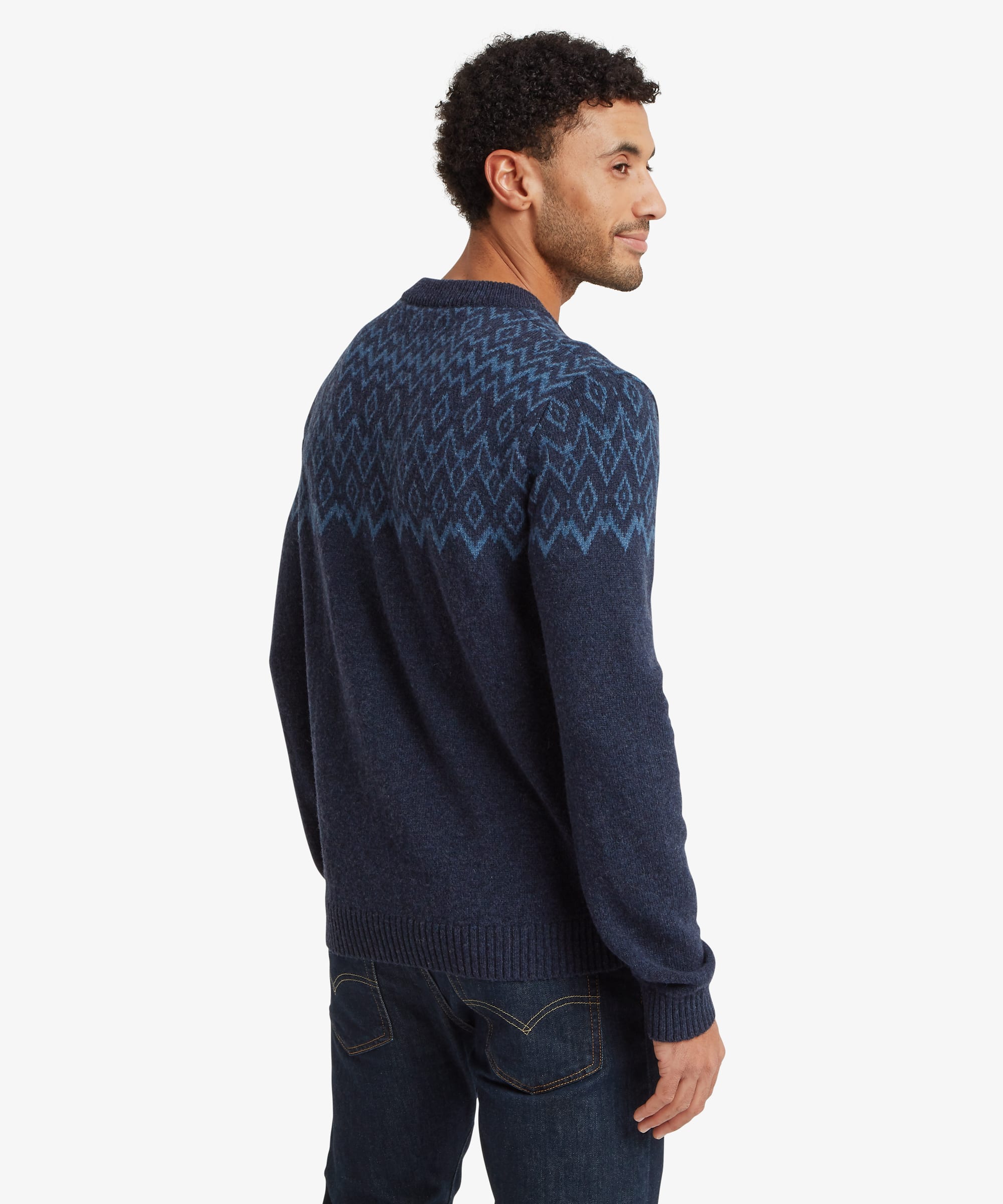 Back view of a man wearing a navy blue sweater featuring a geometric knit pattern across the shoulders and upper back. The regular-fit design is paired with blue jeans and finished with ribbed cuffs, hem and crew neckline.