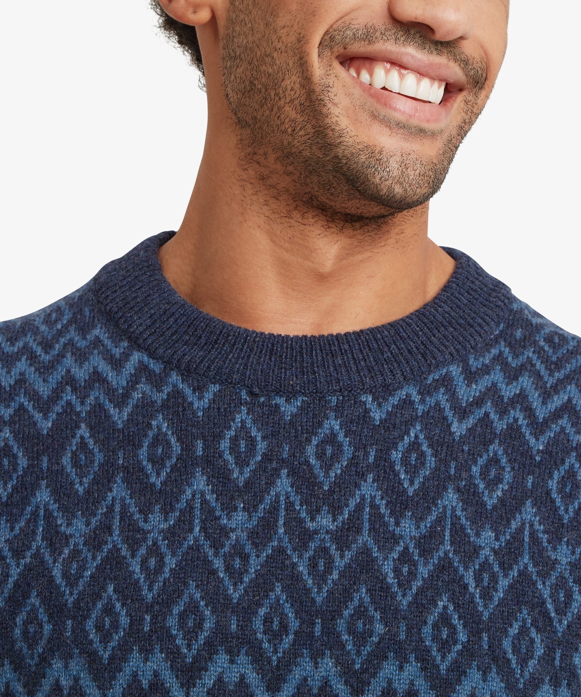 Close-up detail of a navy crew neck sweater showing the textured blue geometric knit pattern across the upper chest. Ribbed neckline construction and the fine knit texture are highlighted in this detailed product shot.