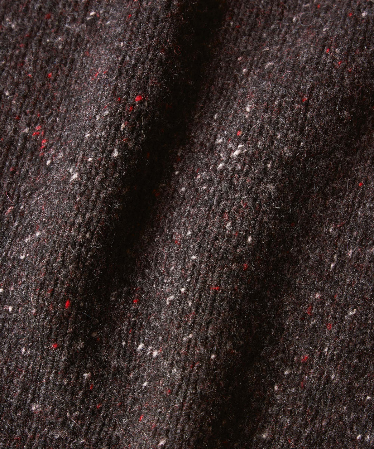 Close-up of a dark charcoal gray knitted fabric with flecks of red and white.