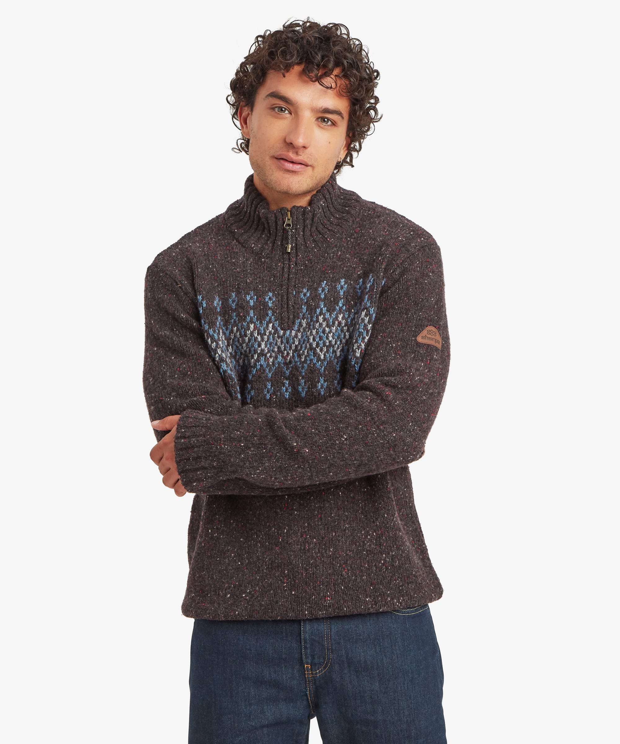 Man wearing a charcoal black quarter-zip knit sweater with a high ribbed collar and a blue, grey and cream geometric Fair Isle-inspired pattern across the chest and upper sleeves. He stands with arms folded, wearing blue jeans. The regular-fit sweater features a contrasting zip placket and a small logo patch on the sleeve.