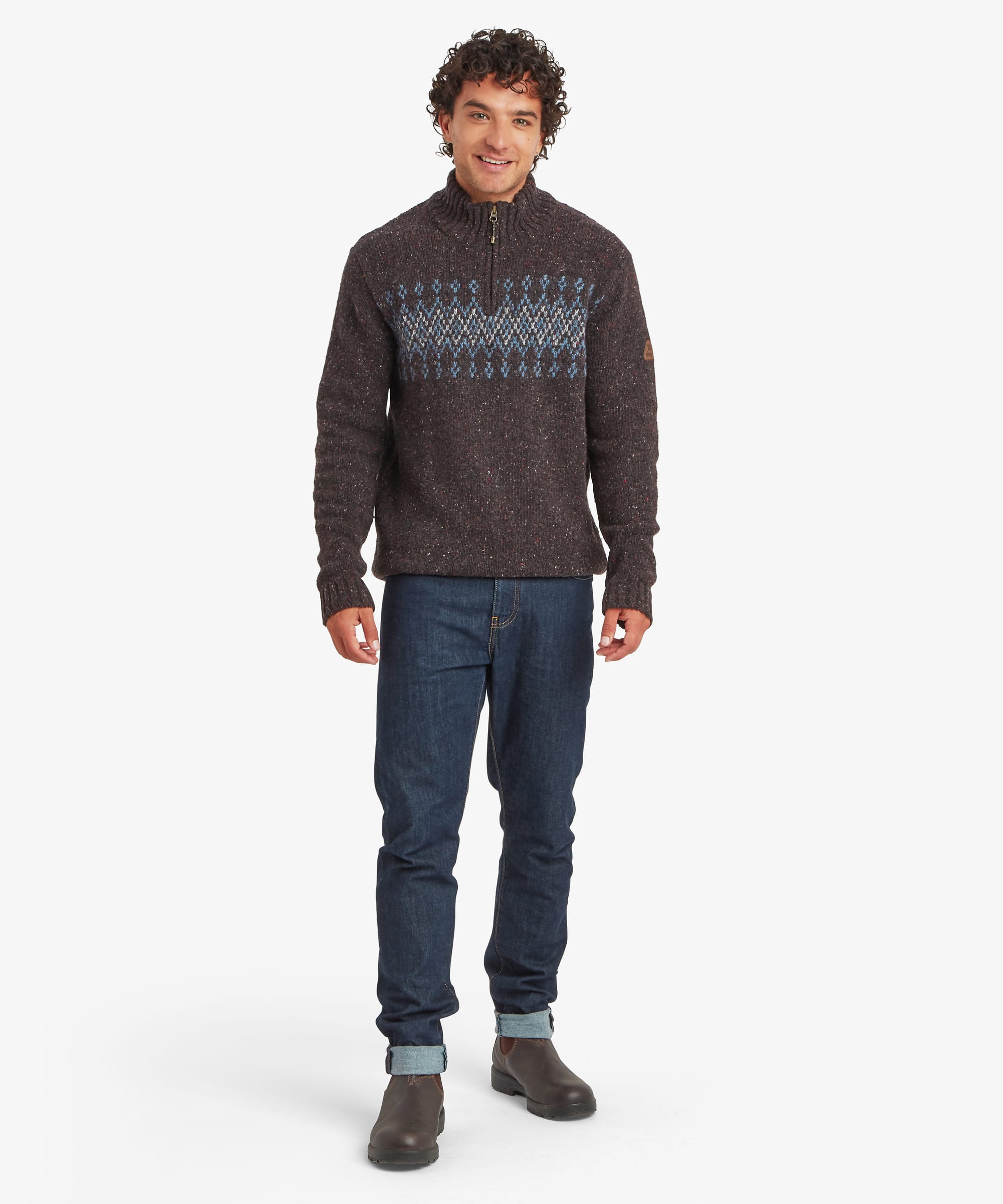 Full-length front view of a man wearing a charcoal black quarter-zip sweater with a patterned chest panel in blue, grey and cream geometric motifs. Styled with blue jeans, the sweater has a regular fit, ribbed cuffs and hem, and a stand collar with a zip fastening.
