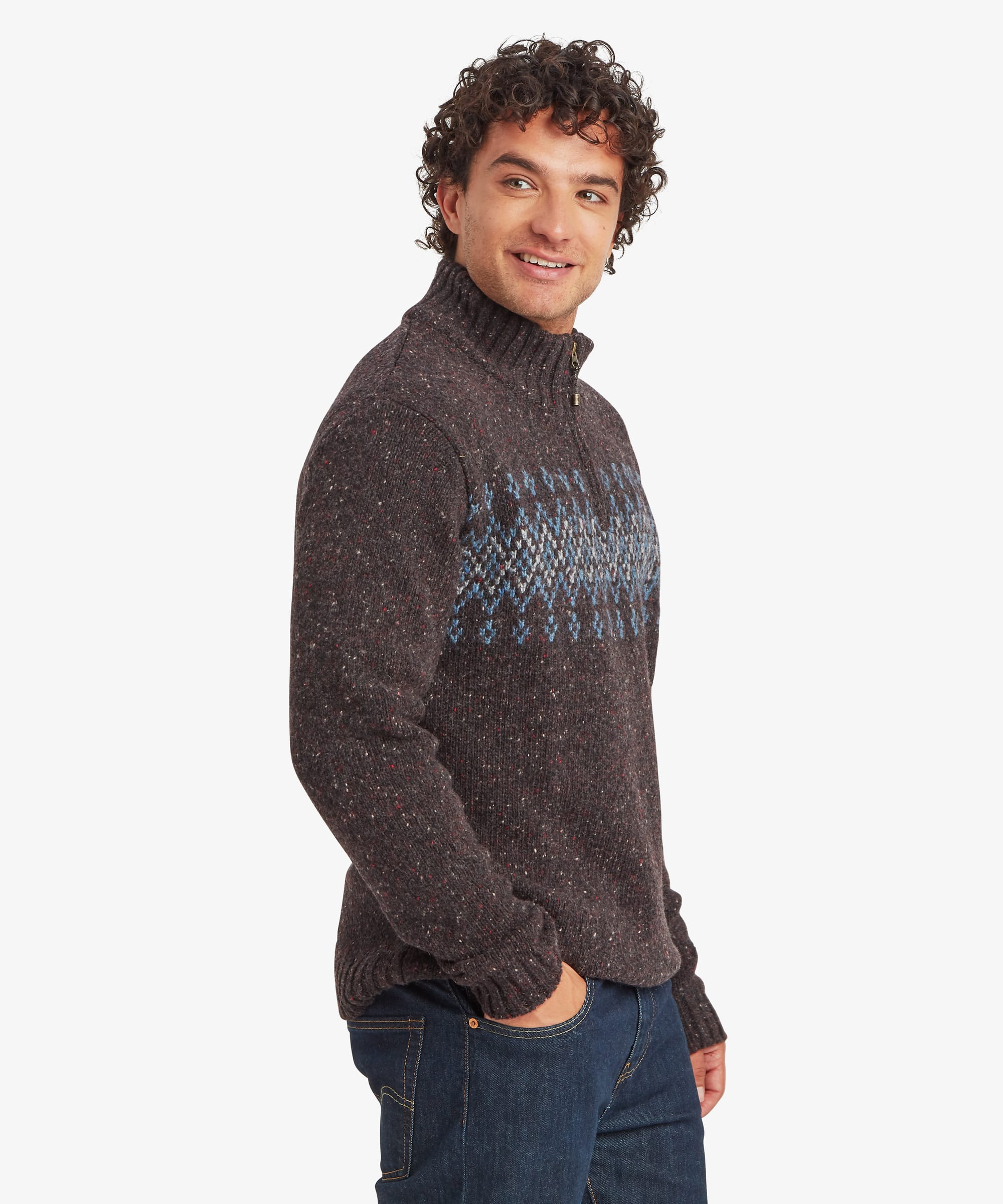 Three-quarter side view of a man smiling while wearing a charcoal black quarter-zip knit sweater. The geometric patterned yoke wraps around the chest and shoulders, while the high collar and contrast zip create a classic outdoor-inspired look. Paired with blue jeans.