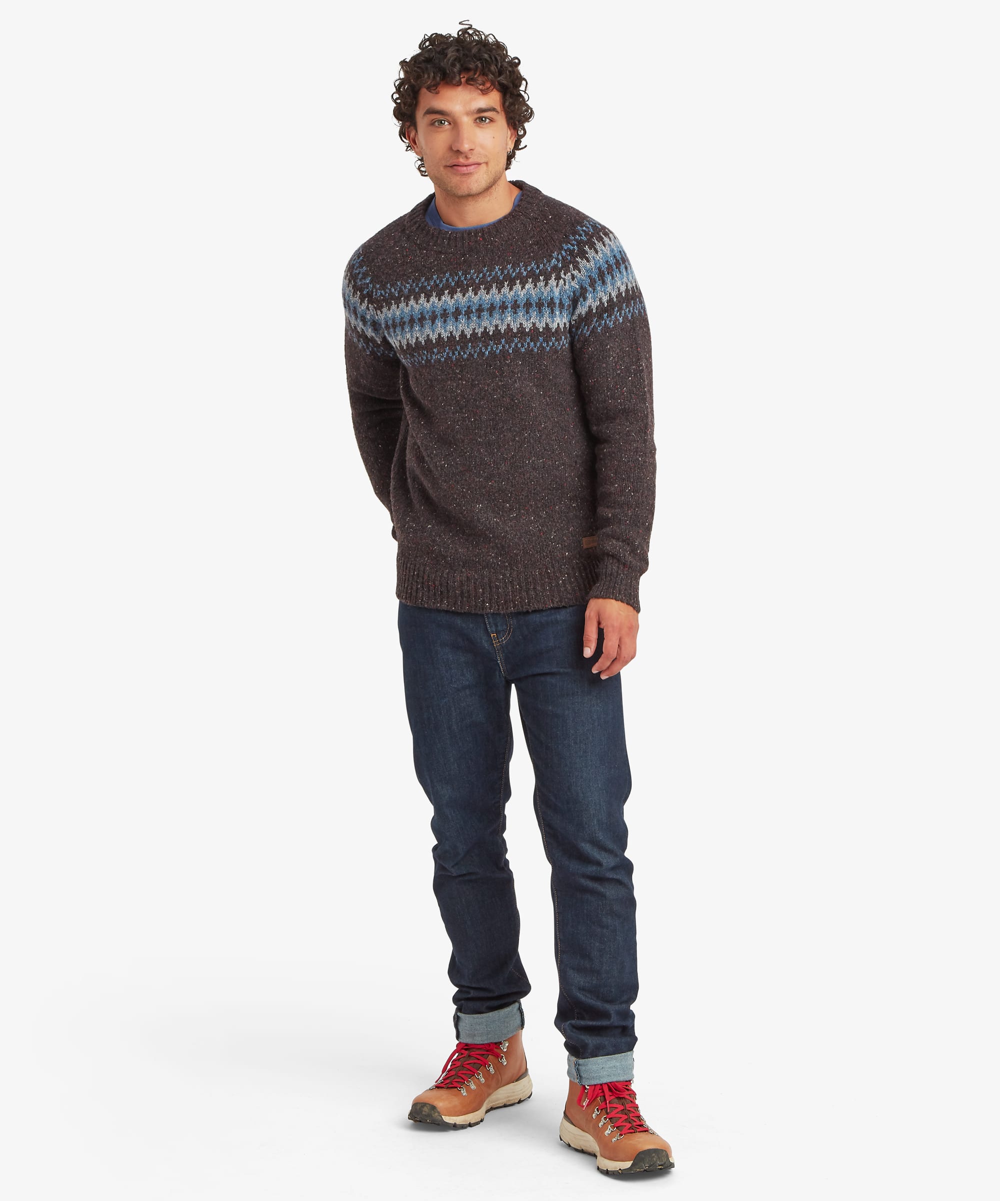 Full-length front view of a man wearing a charcoal black crew neck sweater with a bold blue, grey and white geometric yoke pattern across the upper body. Styled with blue jeans and casual shoes, the regular-fit knit offers a comfortable everyday silhouette.