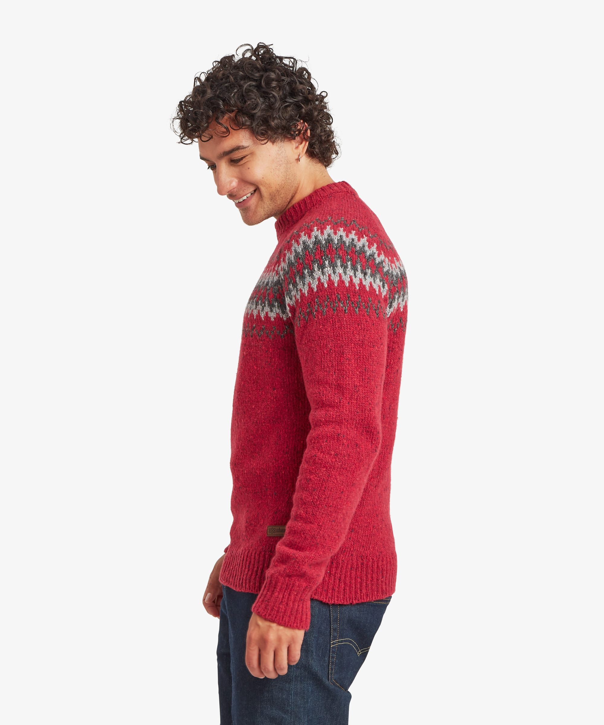 Side profile of a man looking down while wearing a red knit sweater with a Fair Isle-inspired patterned yoke across the upper chest and shoulders. The regular-fit silhouette provides a comfortable fit through the body and sleeves.