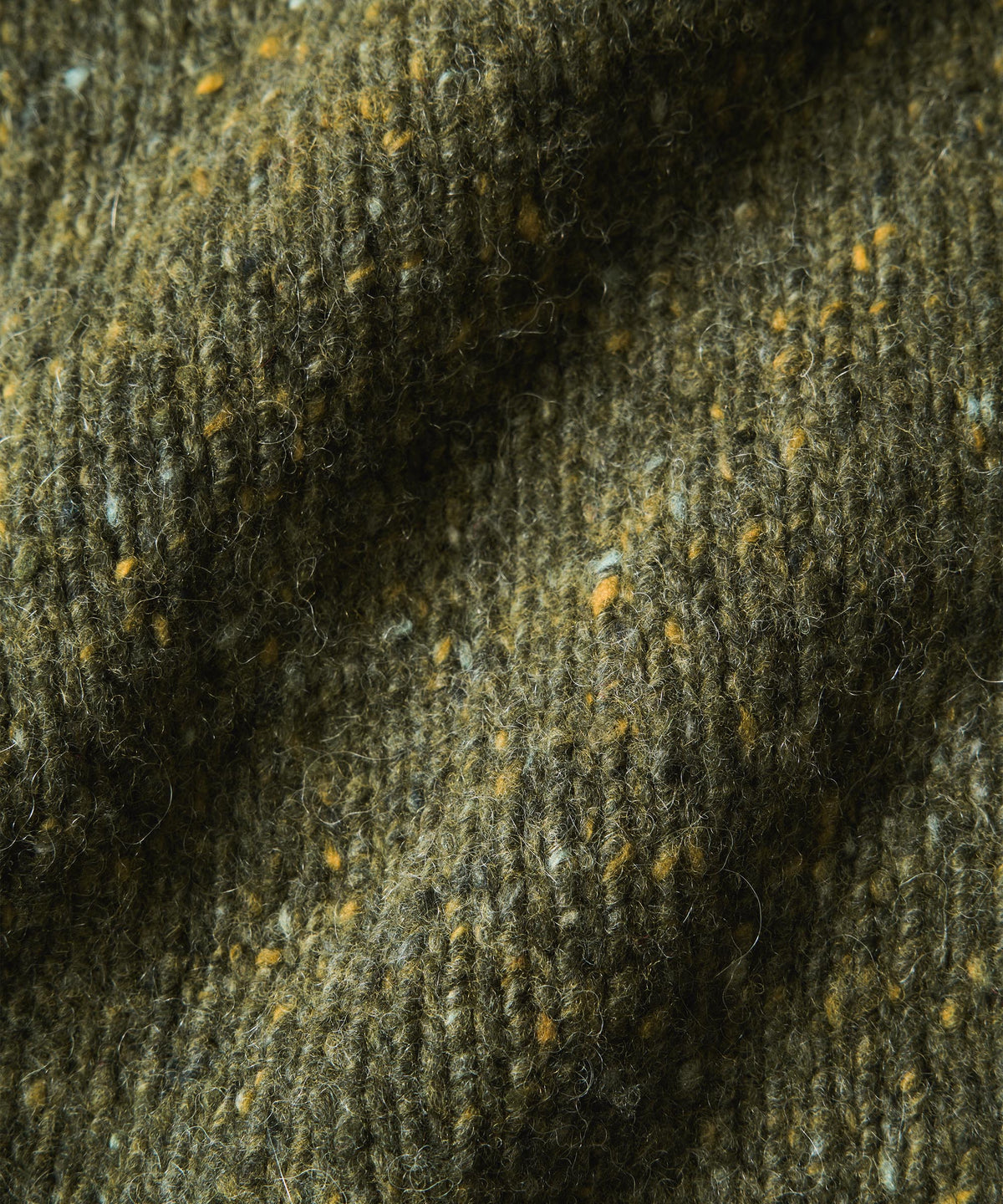 Close-up of a textured knitted fabric in olive green with flecks of yellow, white, and dark brown.