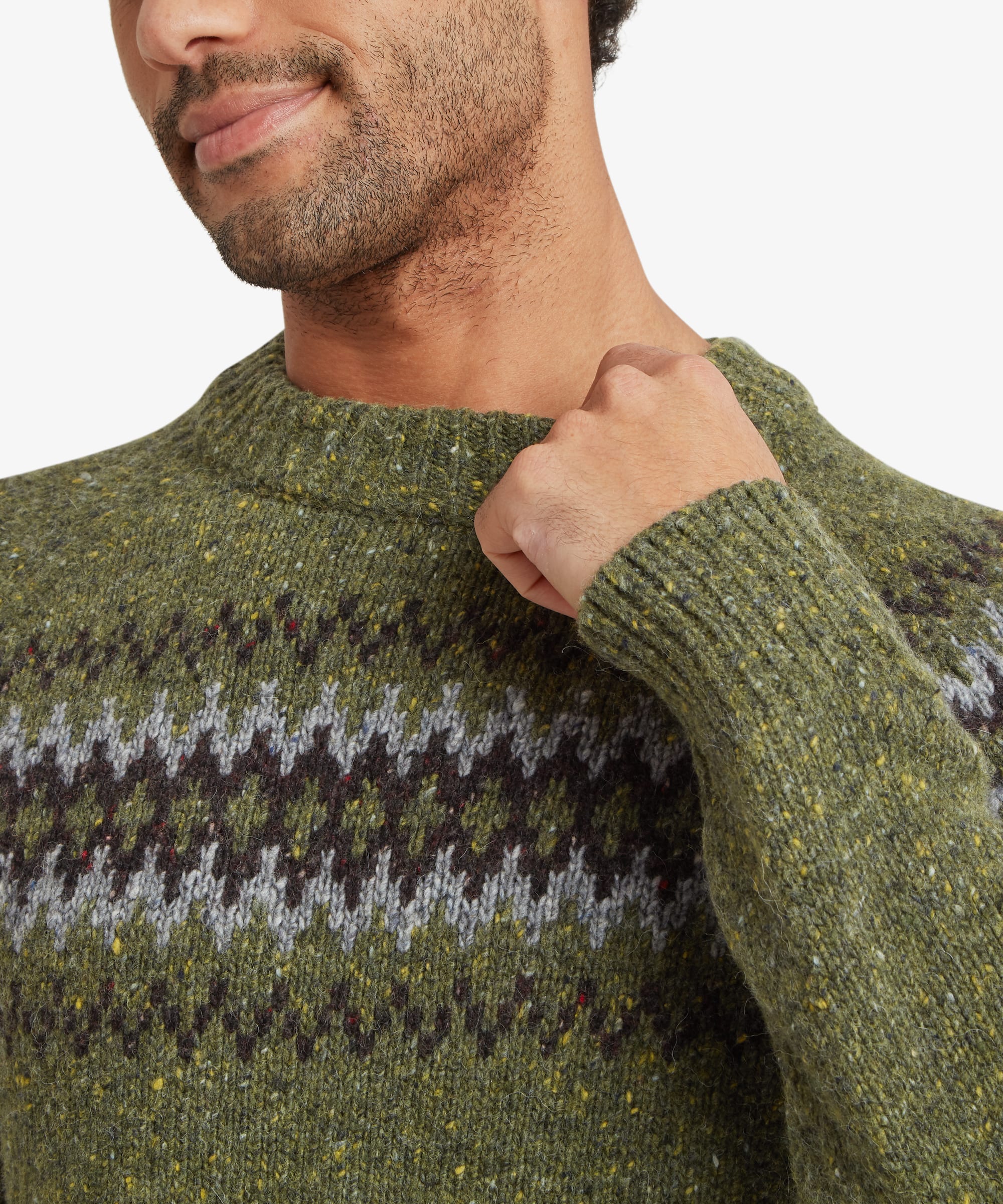 Close-up detail of an olive green crew neck sweater highlighting the textured knit fabric and geometric Fair Isle-inspired pattern in black, grey and cream across the upper chest. The ribbed neckline is clearly visible.