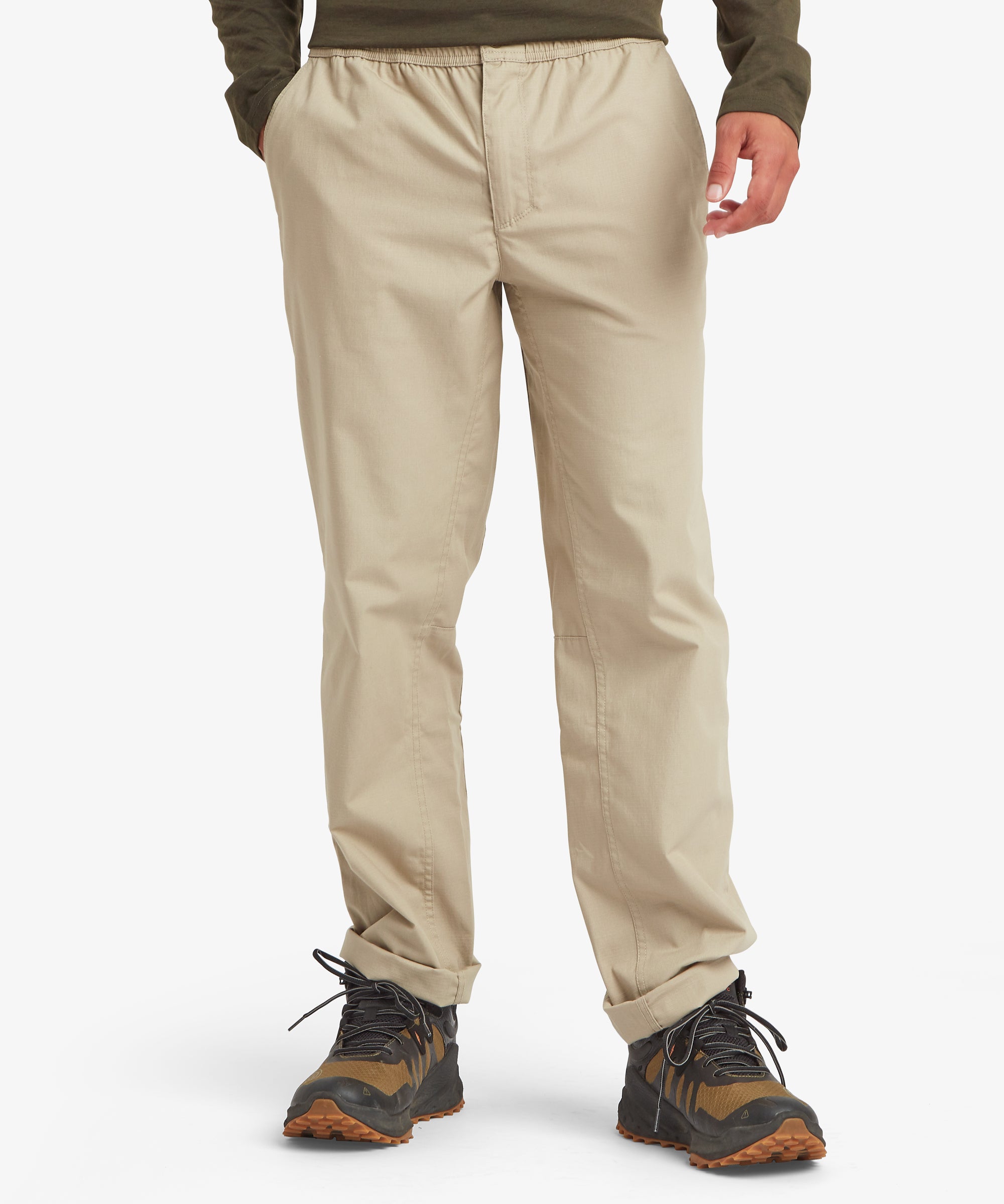 A front view of beige trousers featuring an elastic waistband, side pockets, and straight legs, paired with outdoor hiking shoes.