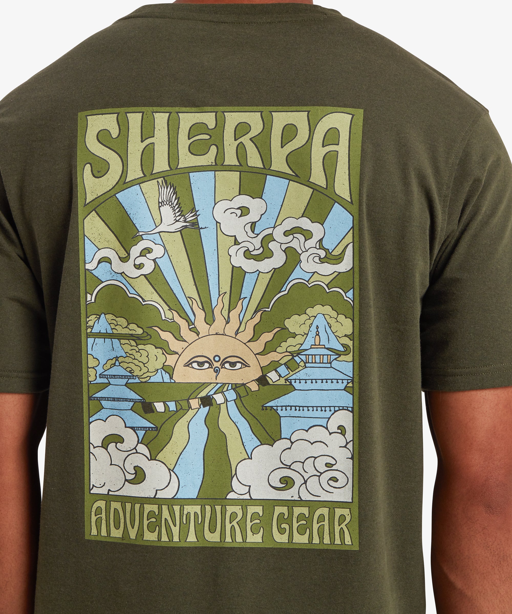 A back view of a man wearing a green short sleeve T-shirt with a pale blue, green and yellow graphic on the back. The vertical rectangular graphic depicts a traditional Nepalese sun at the centre emitting beams of green and blue light. Clouds, traditional Nepali temples and other iconography sit at the adorn the edges of the graphic. The words "Sherpa" is written at the top of the graphic and "Adventure Gear" at the bottom.