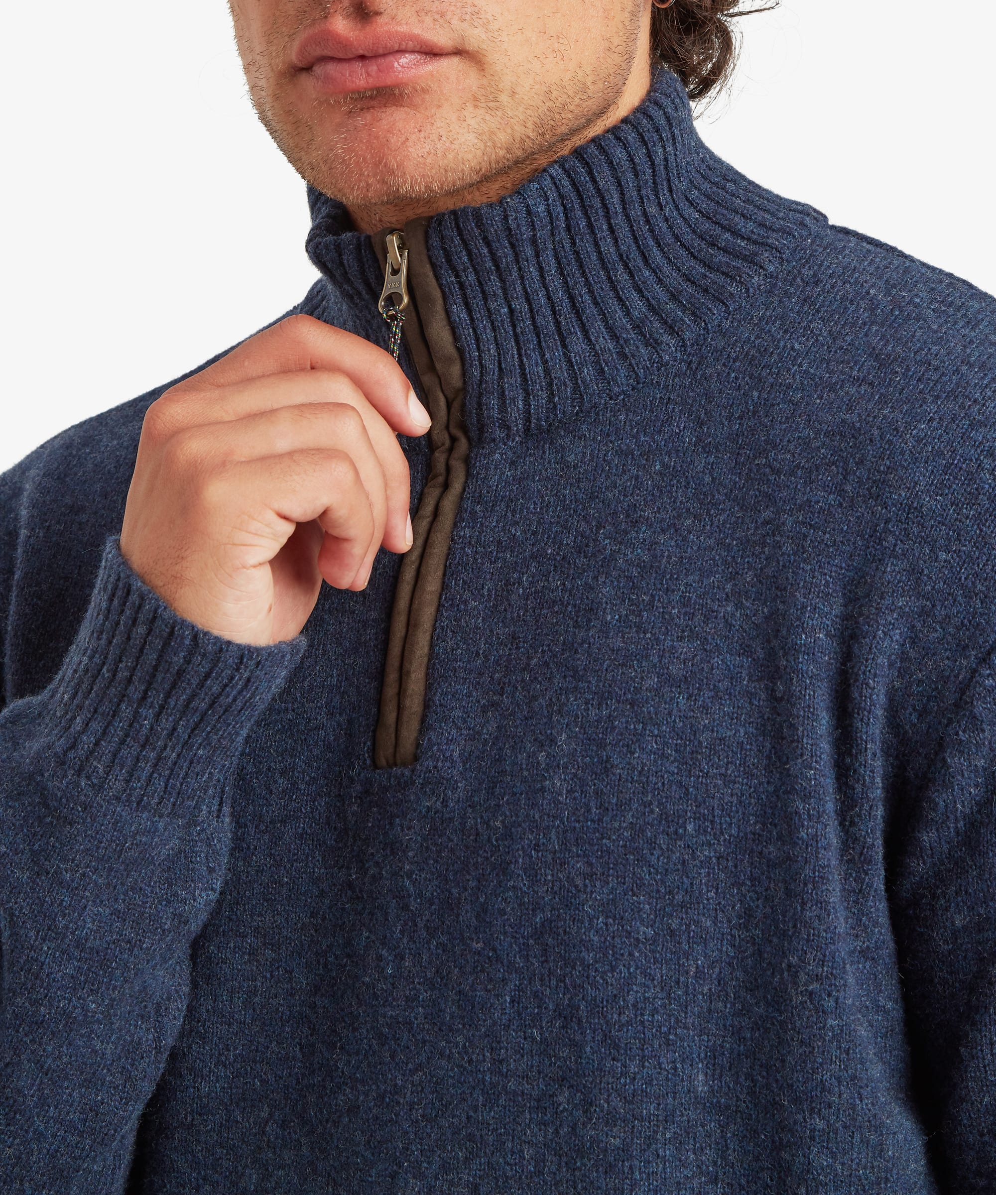 Close-up of a man wearing a navy blue ribbed knit quarter-zip sweater, pulling the zipper slightly with his hand. The zip is finished a fake leather trim and a multi coloured zip puller.