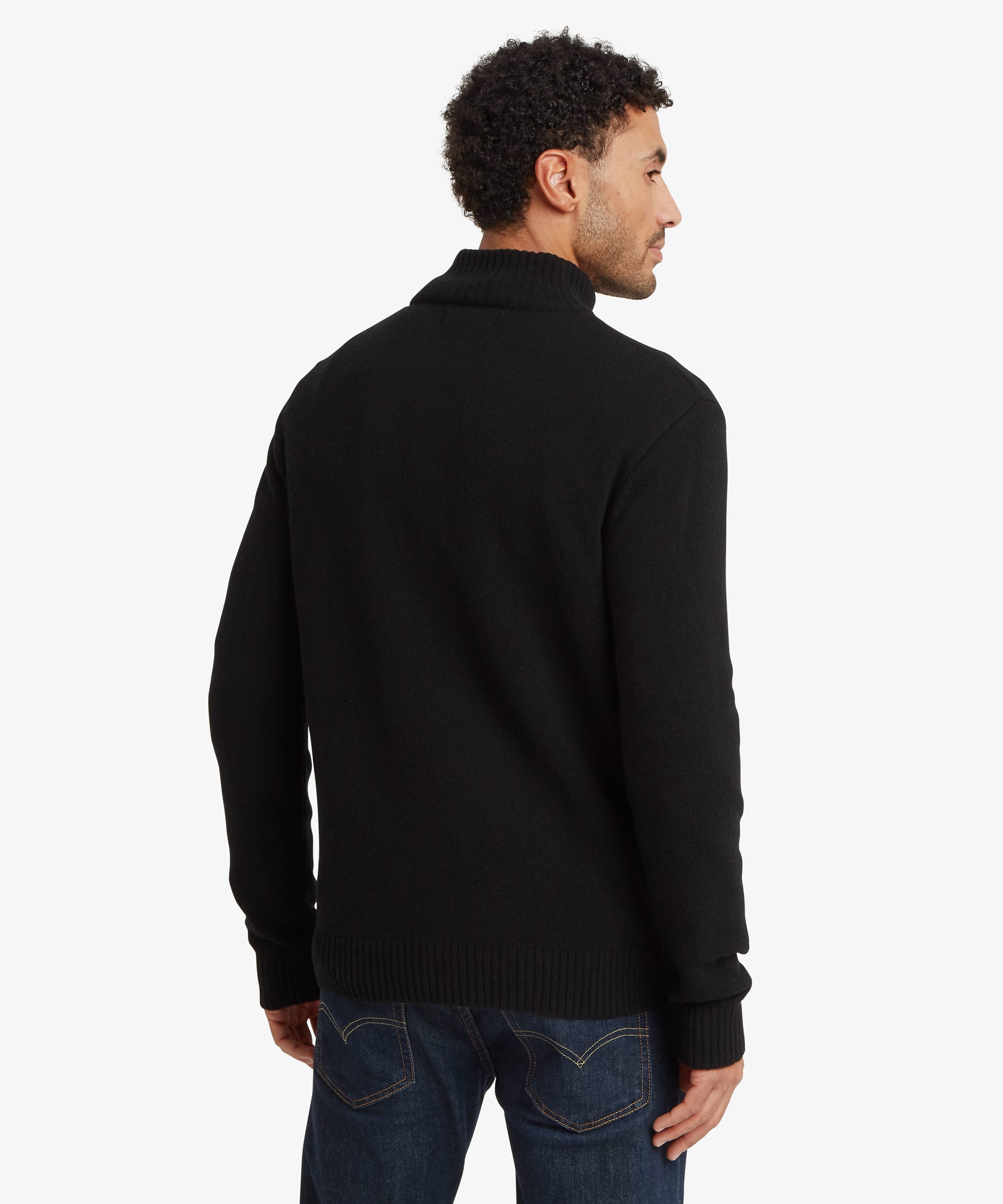 A man wearing a black ribbed mock neck sweater, shown from the back and side profile against a light gray studio background.