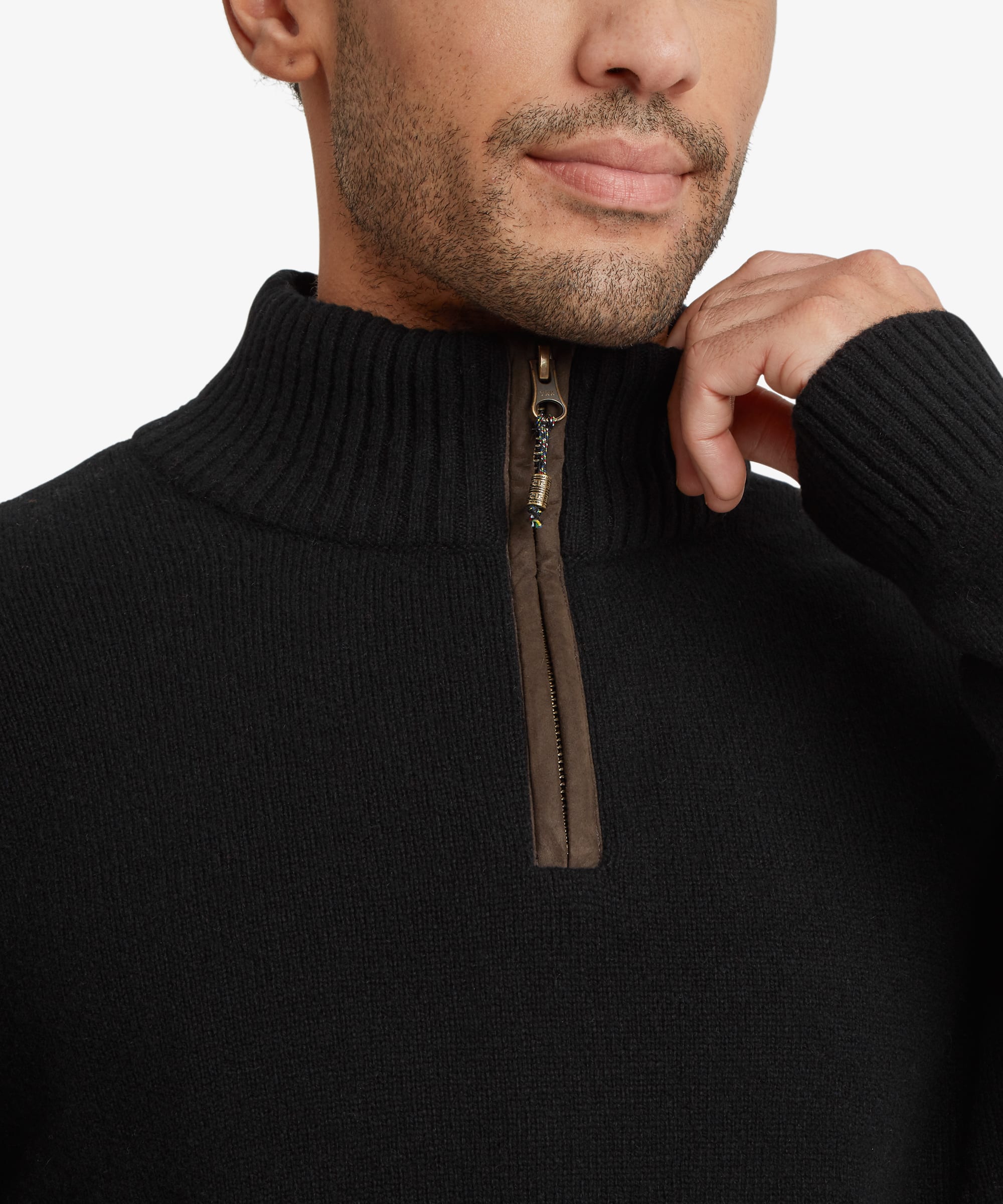 Close-up of a man wearing a black ribbed knit quarter-zip sweater with a brown zipper trim, and a endless knot zip puller against a plain light background.