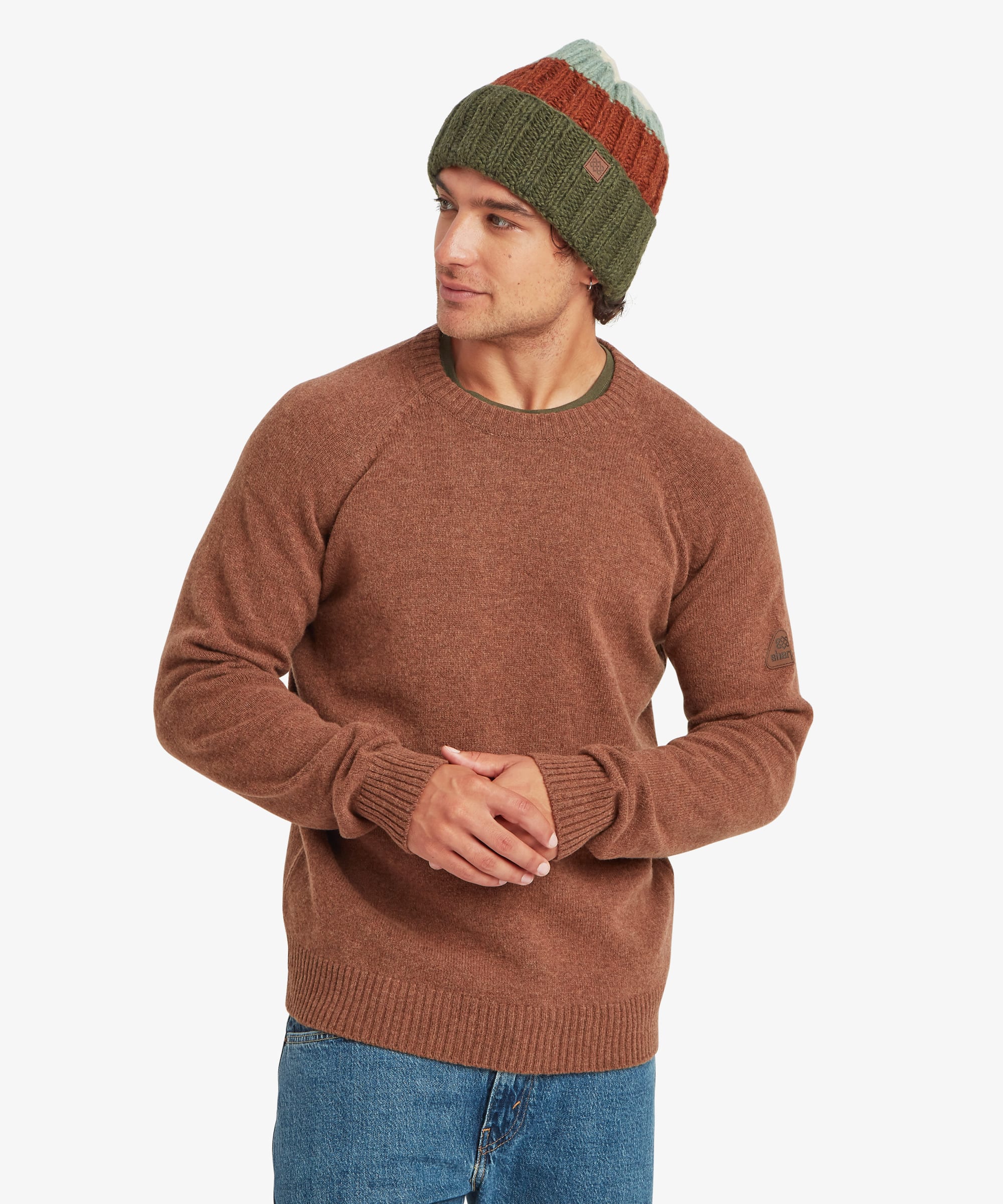 Male model wearing the Sherpa Kangtega Crew Sweater in brown with blue jeans and a green striped knit beanie, shown from the front. The sweater features a classic crew neckline, long sleeves, and a clean, regular fit with ribbed cuffs and hem.