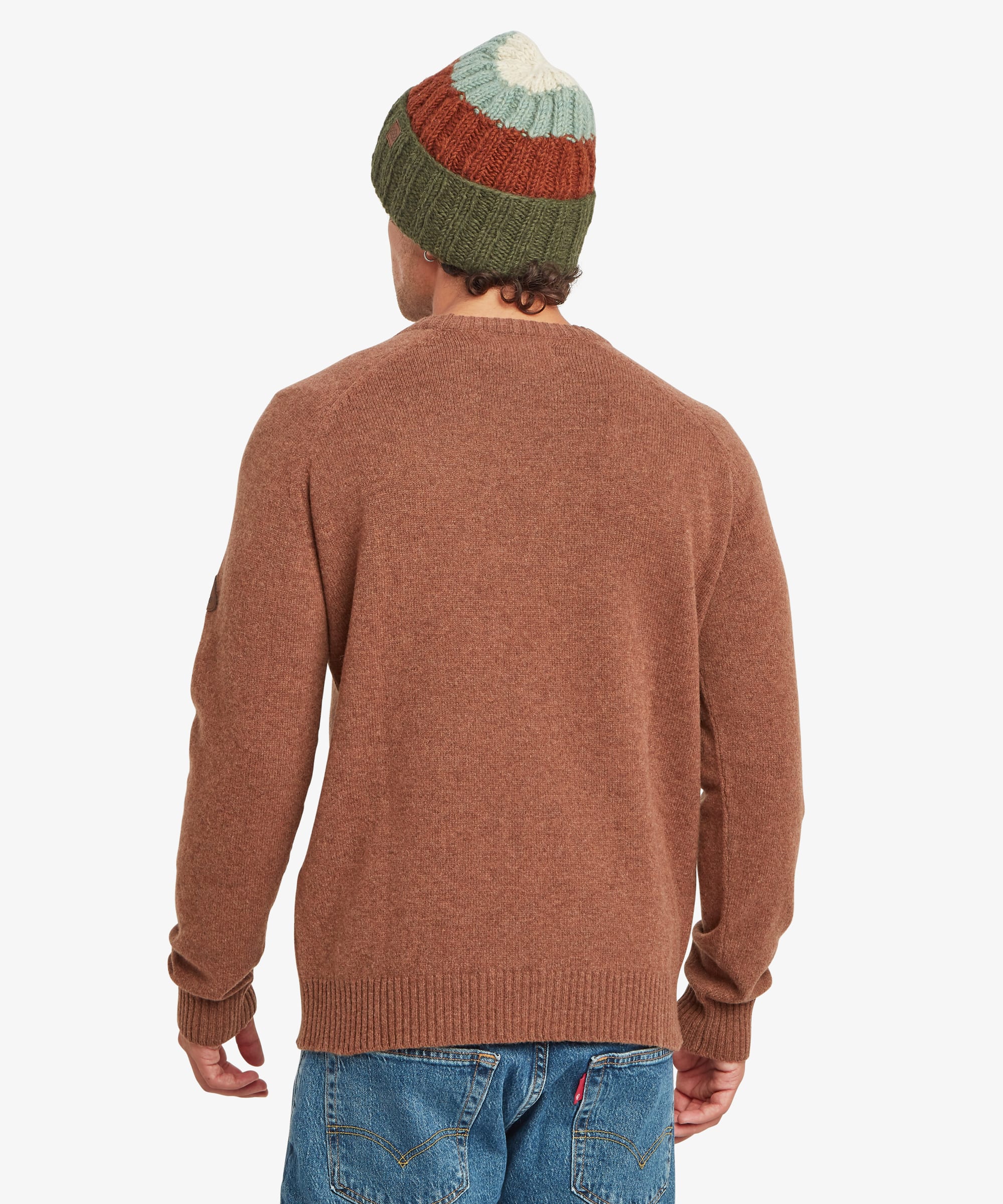 Rear view of a male model wearing the Sherpa Kangtega Crew Sweater in brown with blue jeans and a green striped knit beanie, showing the plain back, long sleeves and ribbed hem.
