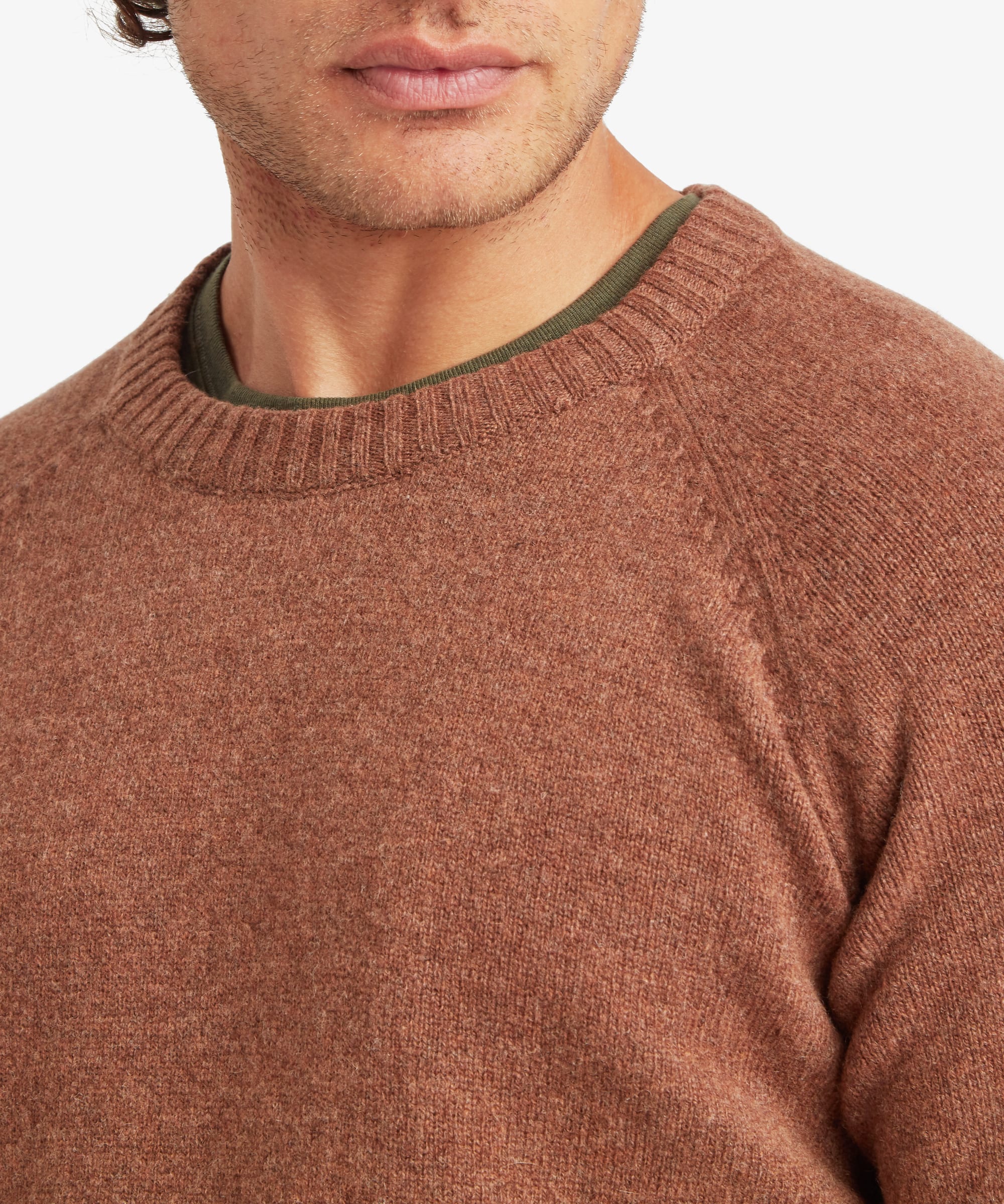 Close-up of the upper body showing the Sherpa Kangtega Crew Sweater in brown on a male model, highlighting the soft knit texture, classic crew neckline, raglan sleeve construction and subtle marl finish.