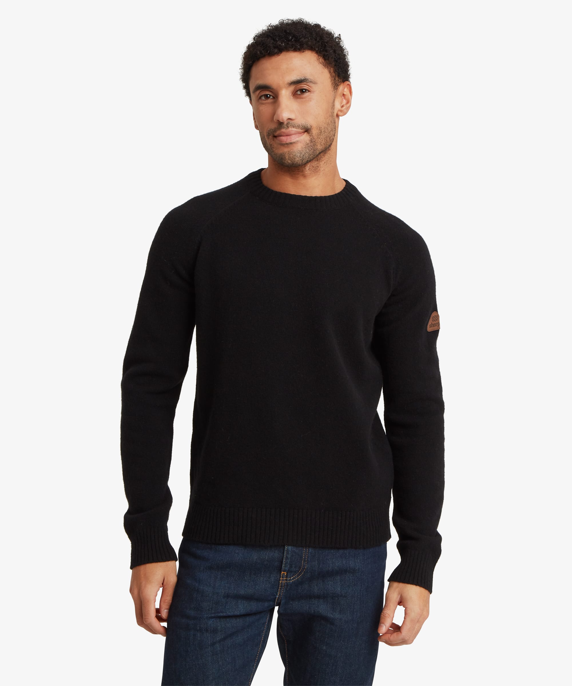 Male model wearing the Sherpa Kangtega Crew Sweater in black with dark blue jeans, shown from the front. The sweater features a timeless crew neckline, long sleeves, ribbed cuffs and hem, and a clean regular fit.