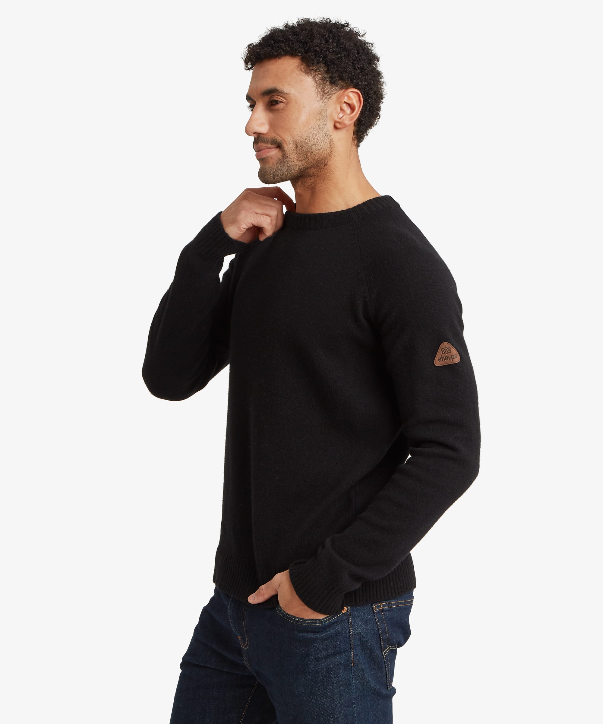 Three-quarter side view of a male model wearing the Sherpa Kangtega Crew Sweater in black with dark blue jeans, highlighting the clean fit, crew neckline and long sleeves.